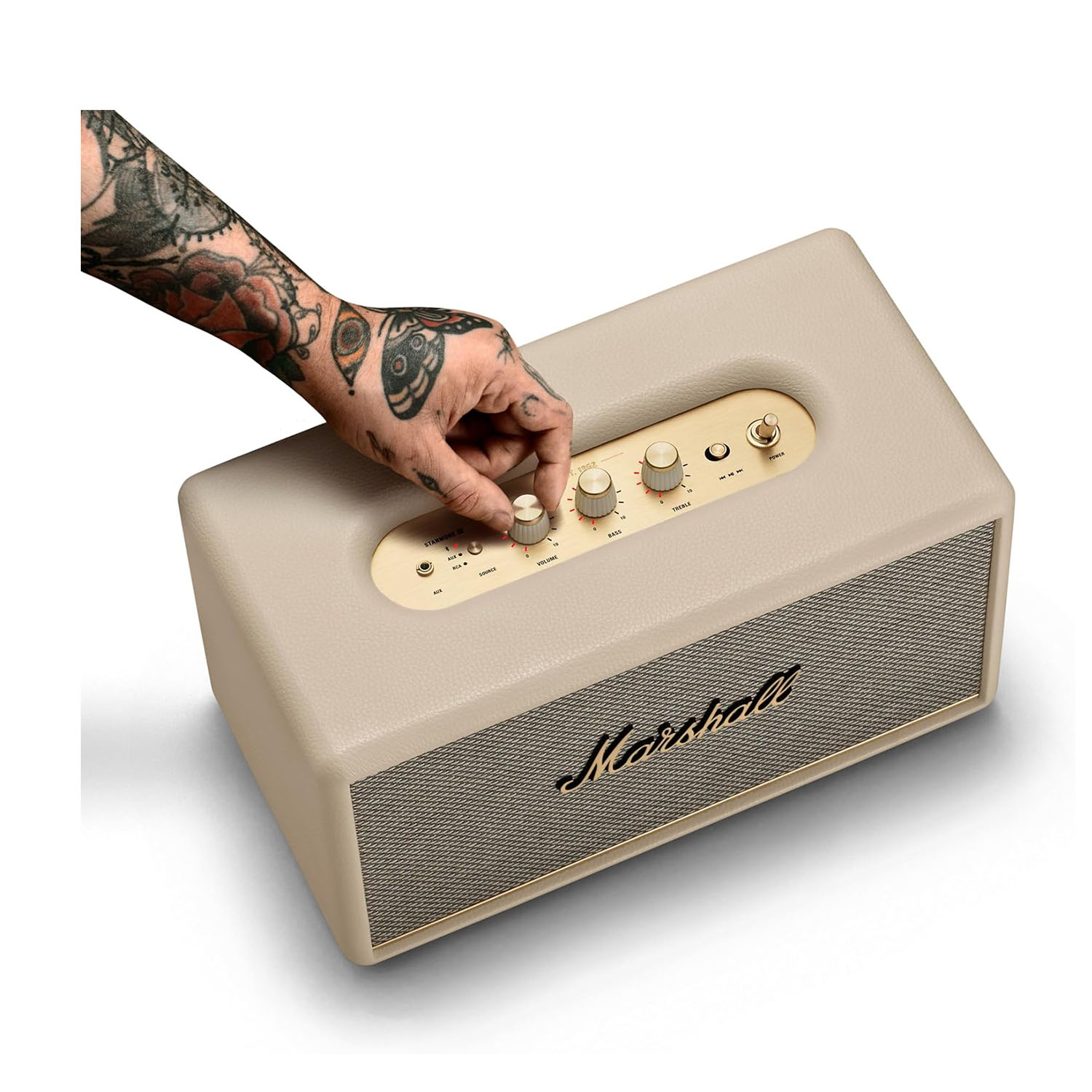 Eine Hand mit Tätowierungen dreht einen Knopf an einem beigen Marshall-Lautsprecher.