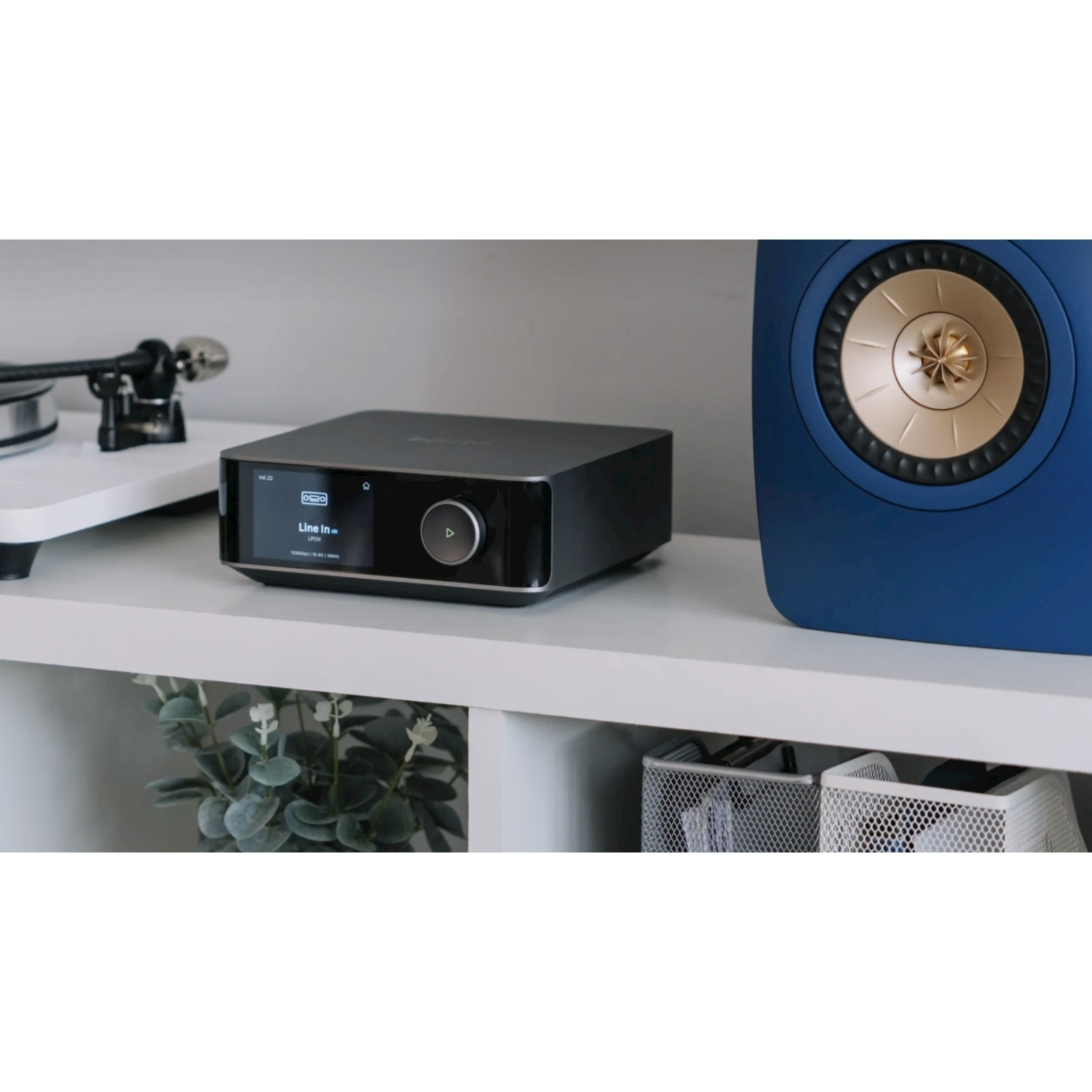 Ein schwarzer Audioplayer steht neben einem blauen Lautsprecher auf einem Regal.