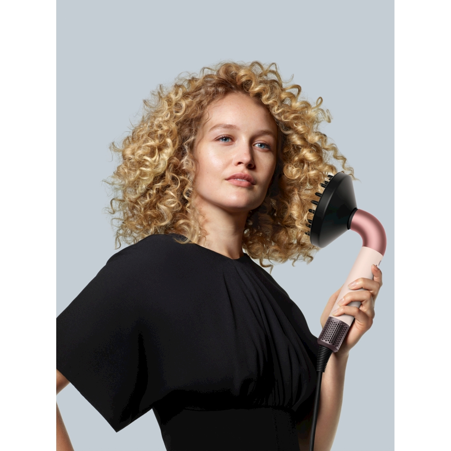 Eine Frau mit lockigem Haar hält einen Haartrockner mit Diffusor.