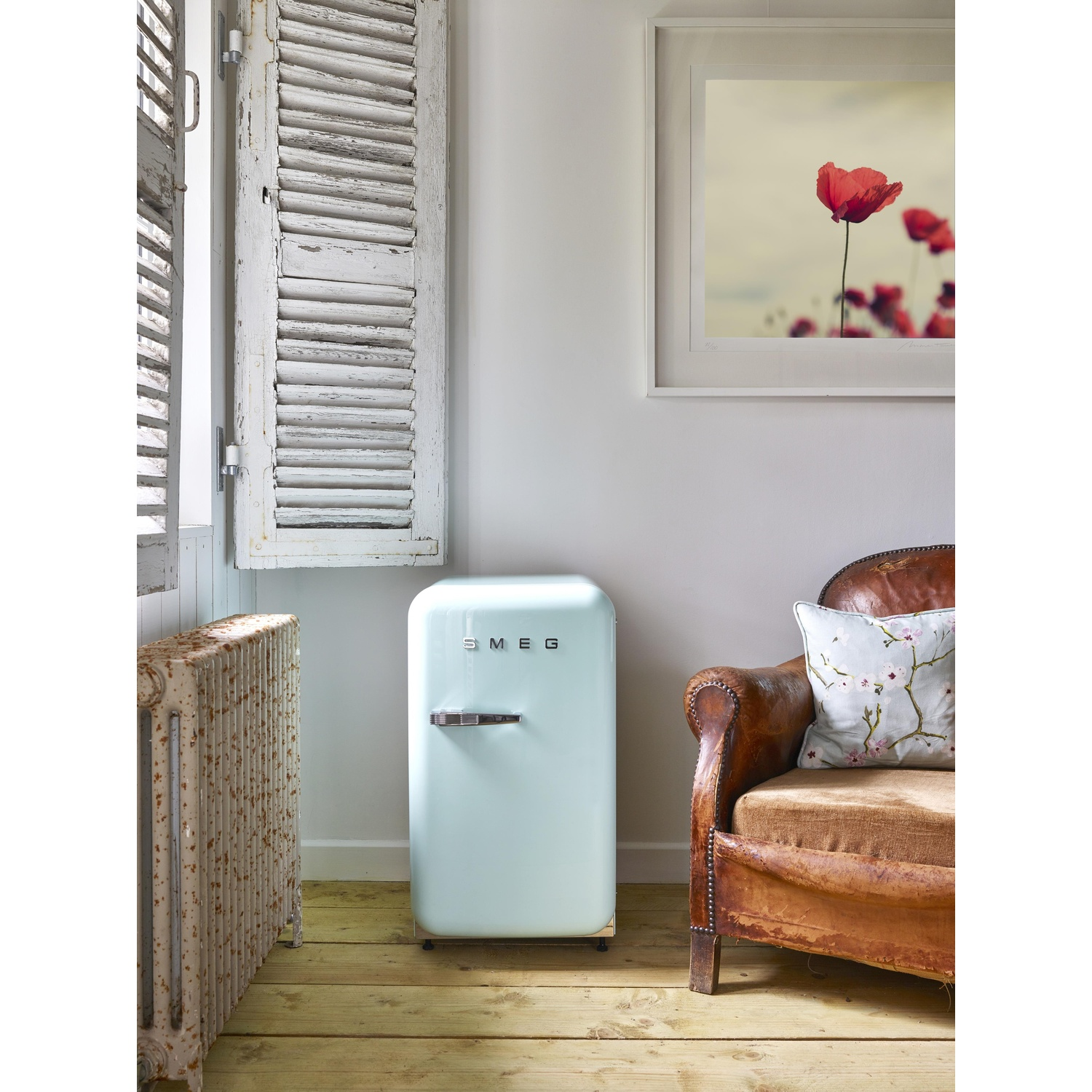 Un refrigerador Smeg azul claro junto a un sillón de cuero marrón.