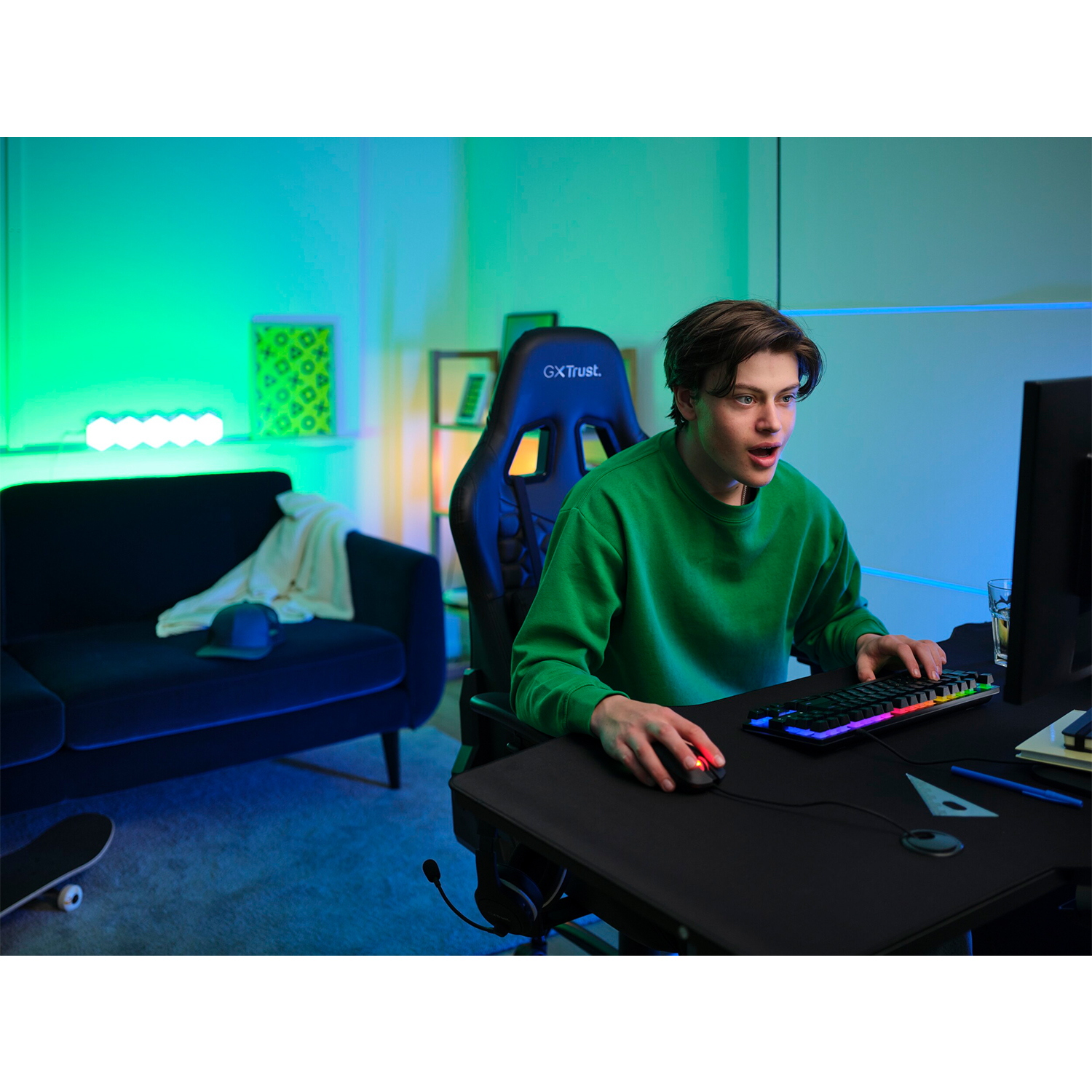 Un giovane in maglione verde gioca al computer, illuminato dalle luci RGB della tastiera.