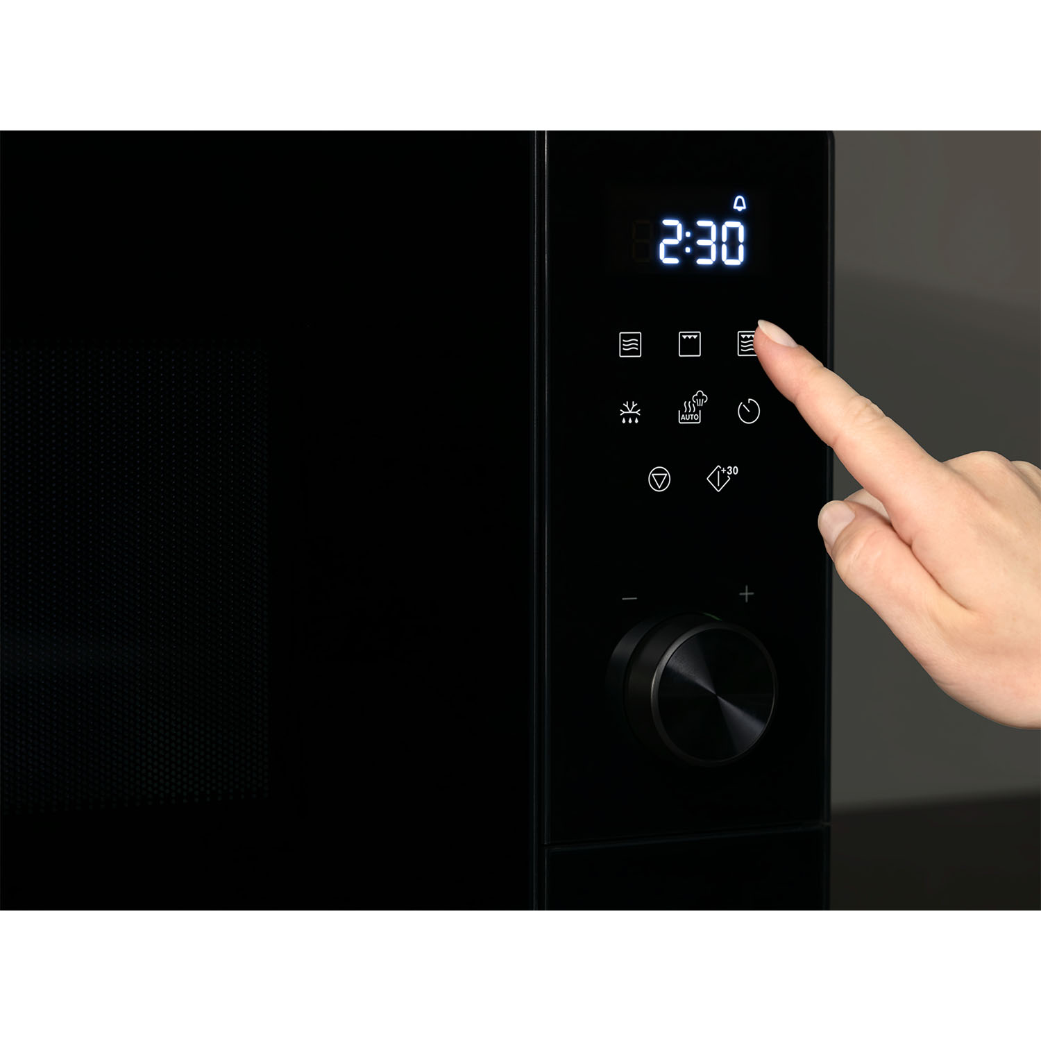 Eine Hand drückt auf die Tasten eines schwarzen Mikrowellen-Bedienfelds mit digitaler Anzeige.