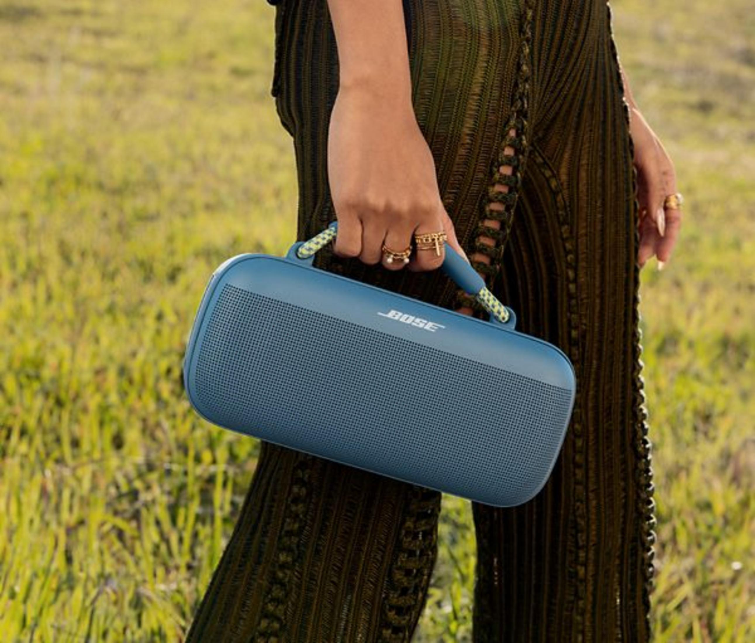 Una persona tiene un altoparlante Bose blu in un campo erboso.