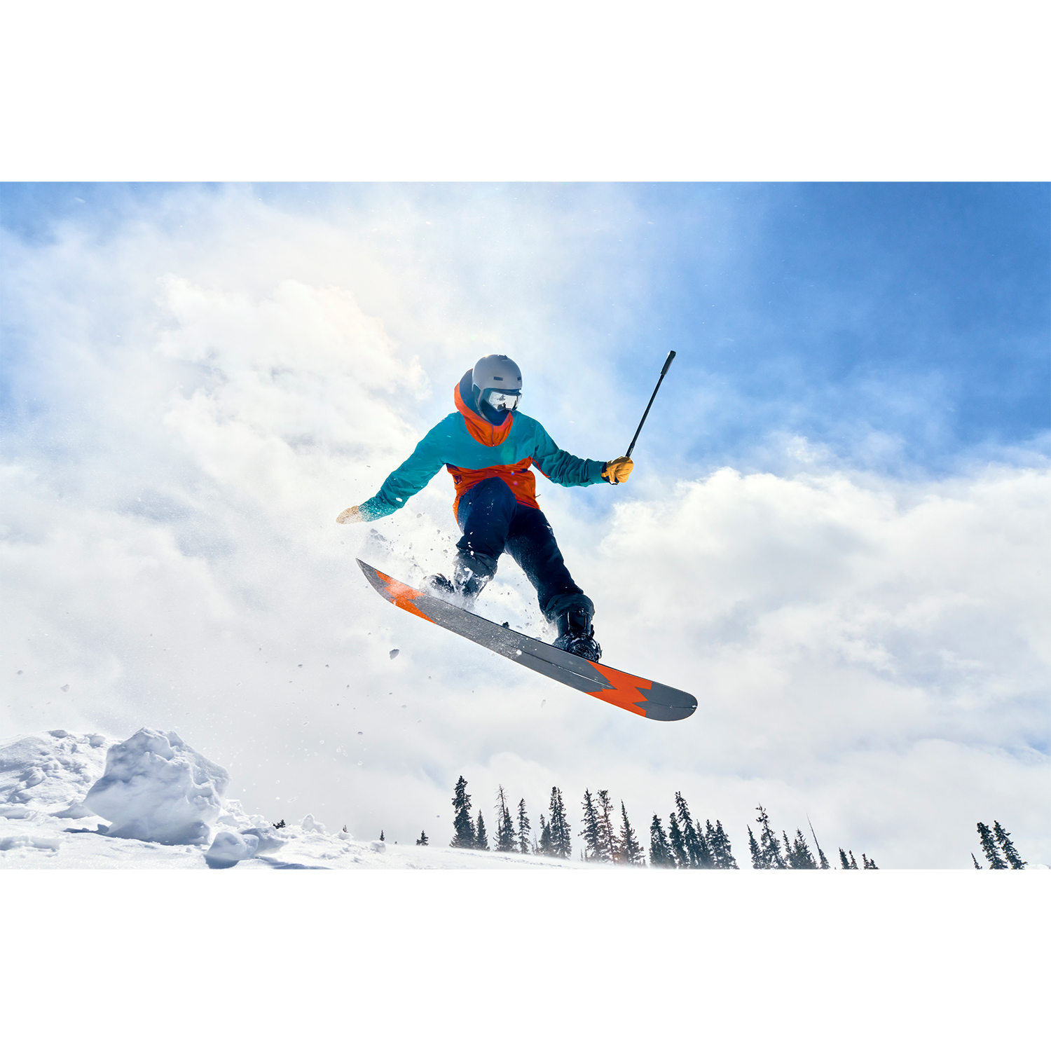 Snowboarder w powietrzu na tle błękitnego nieba z chmurami.
