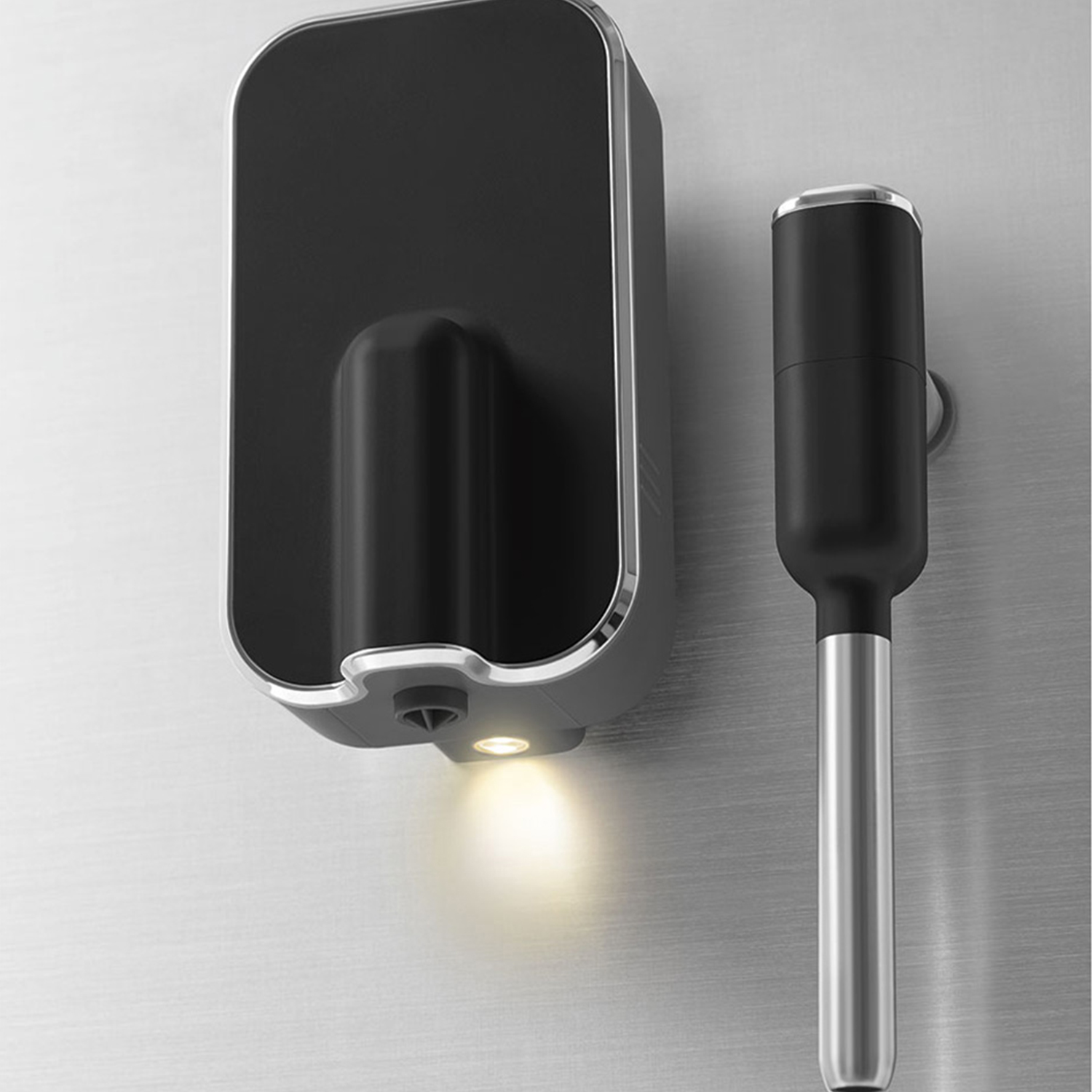 Czarny dozownik mydła ze światłem i blender ręczny ze srebrną rączką na ścianie.