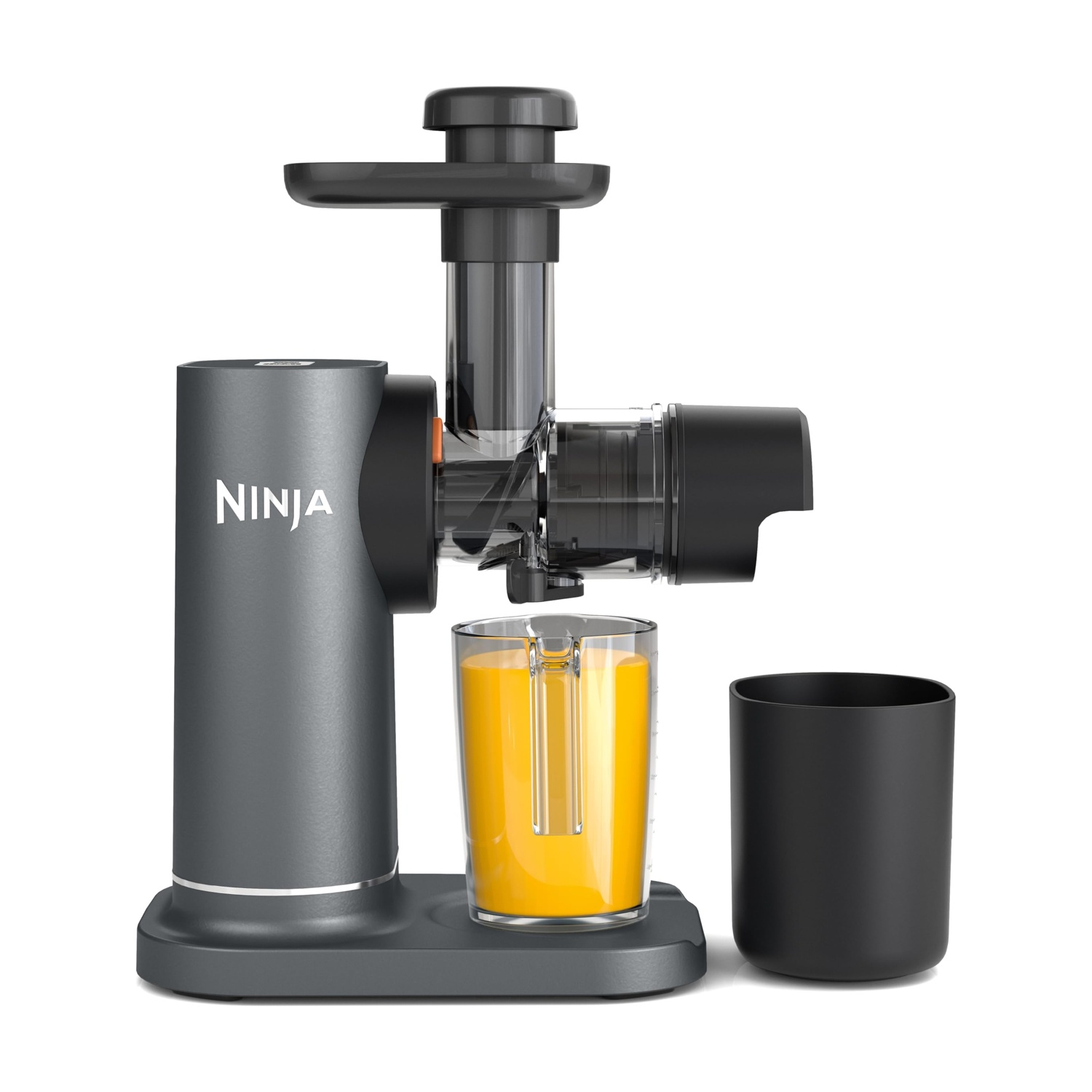 Ein grauer Ninja Entsafter mit einem Glas Orangesaft und einem schwarzen Behälter daneben.