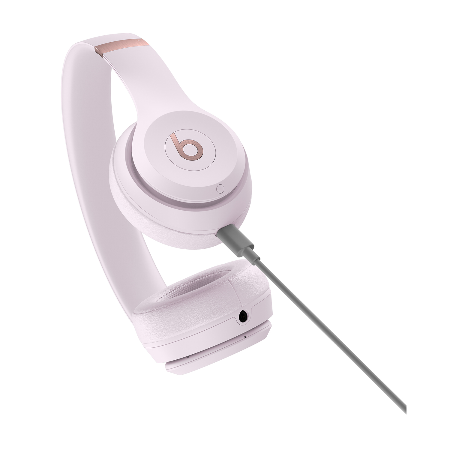 Jasnoróżowe słuchawki z logo 'b' w kolorze różowego złota i szarym kablem.