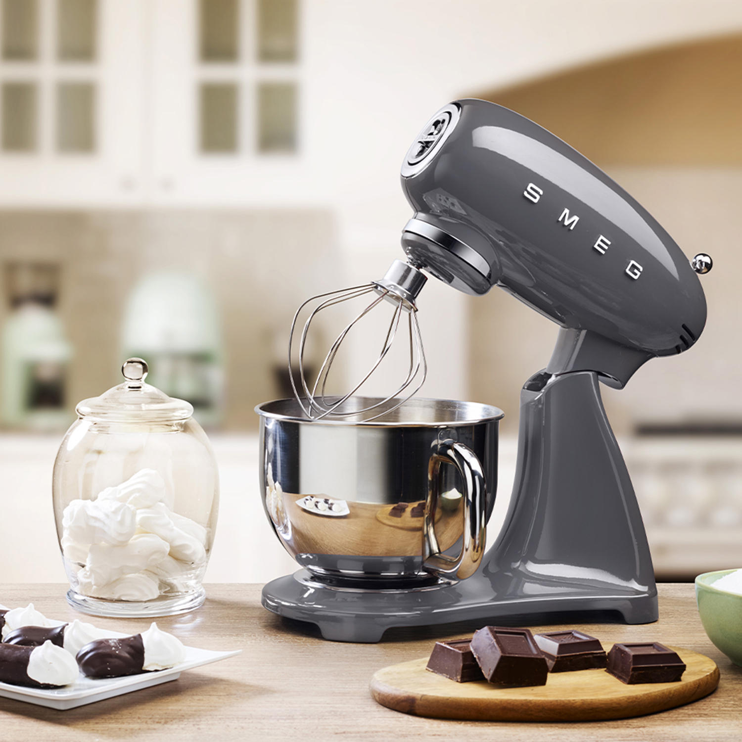 Sbattitore Smeg grigio con frusta, accanto a un barattolo di vetro con meringhe e cioccolato.
