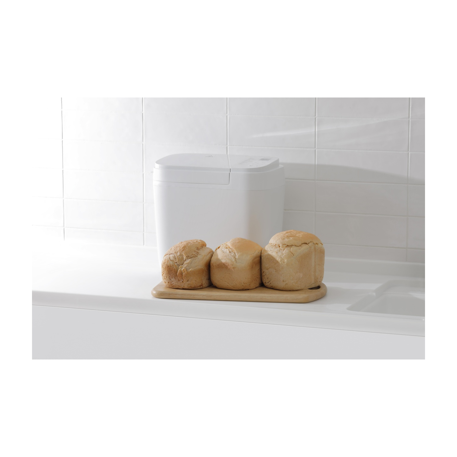 Een witte broodbakmachine staat achter drie broden op een snijplank.