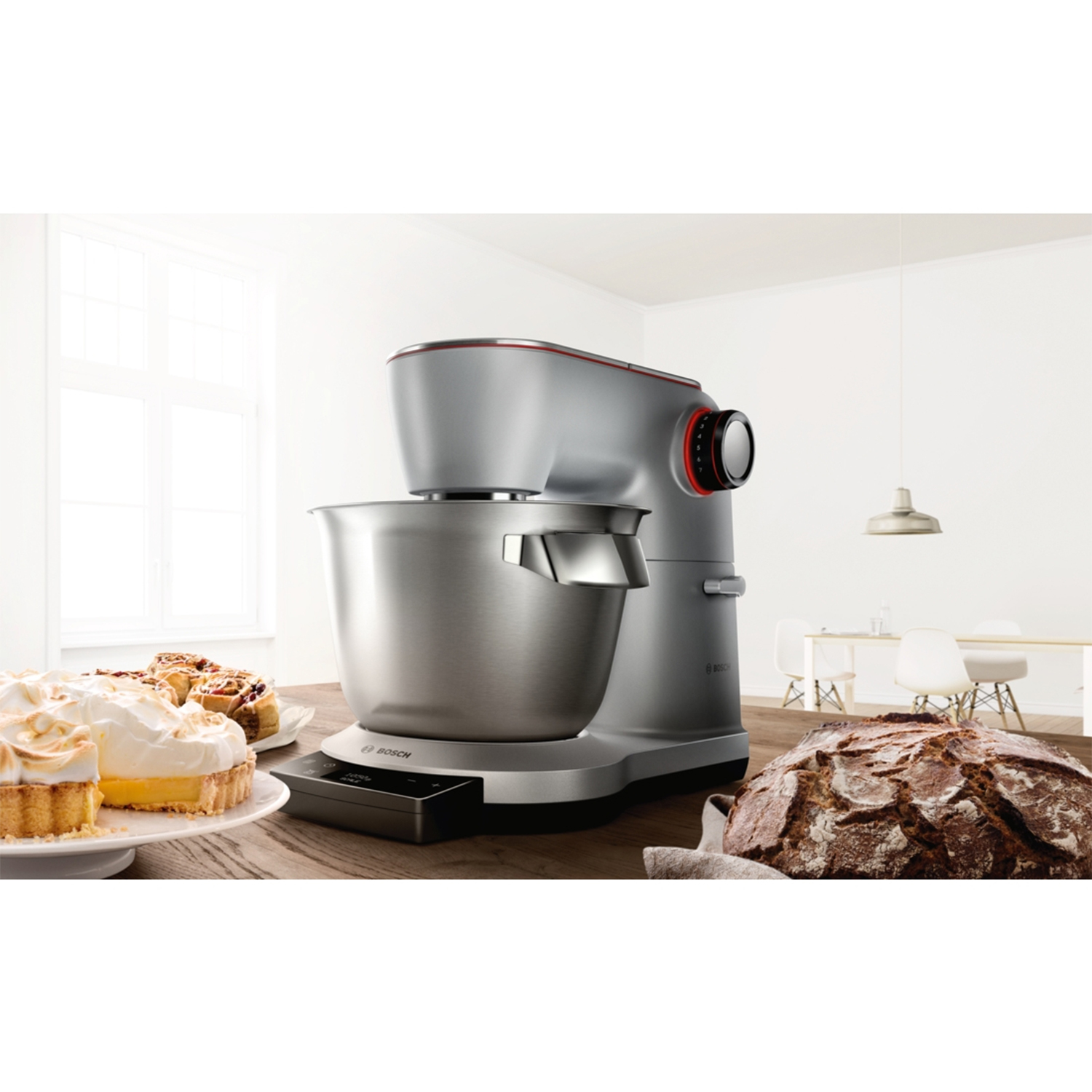 Un robot da cucina argento su tavolo di legno vicino a torte e pane.