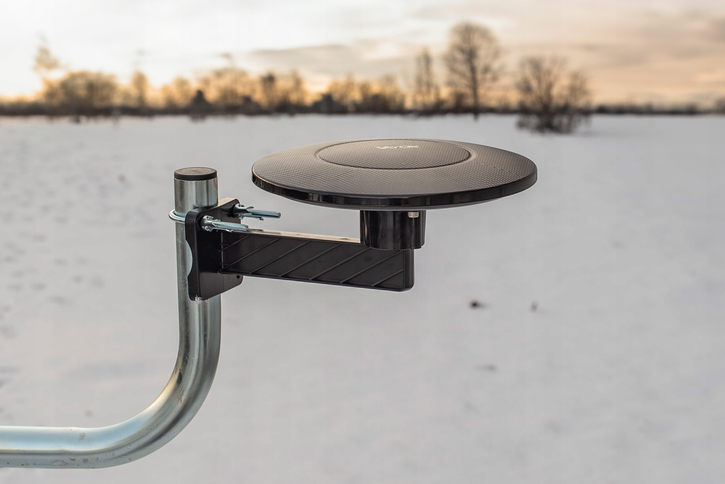 Czarny, okrągły odbiornik satelitarny na metalowym słupku w śniegu.