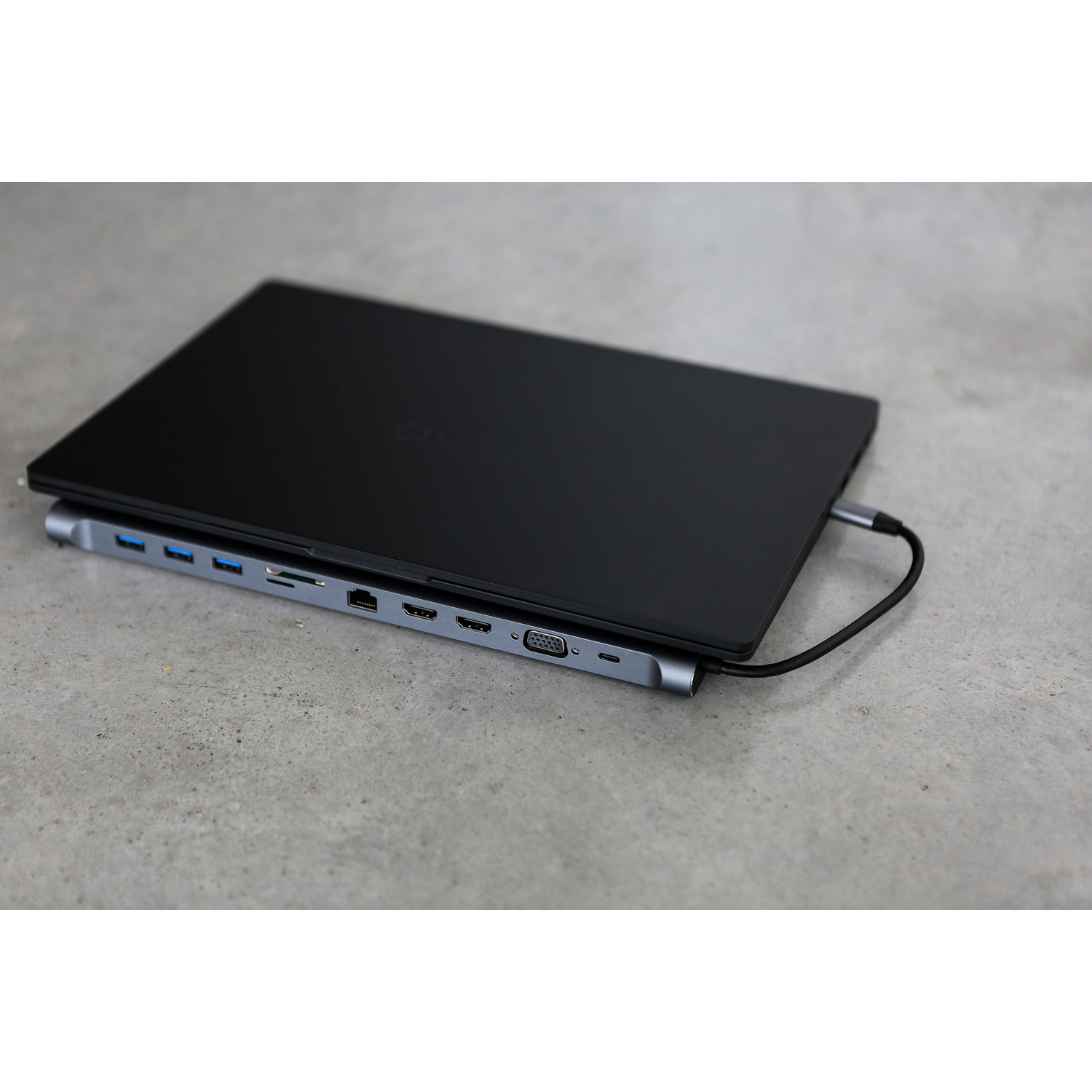 Ein schwarzer Laptop mit angeschlossenem Docking-Hub auf Beton.