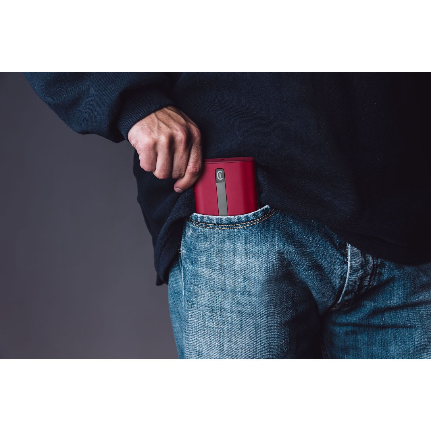 Eine Hand steckt ein rotes Gerät in eine Jeanstasche.