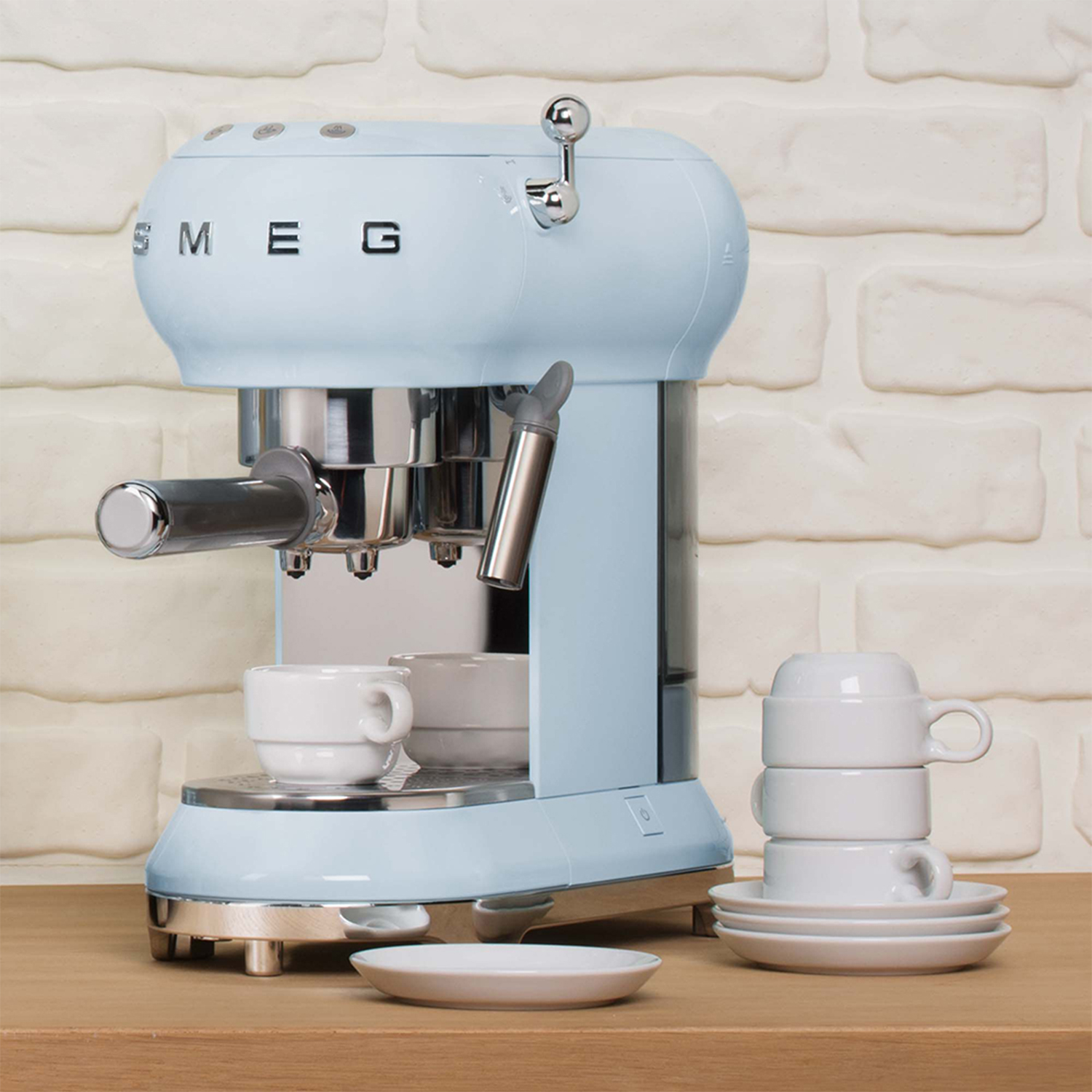 Una macchina per espresso Smeg azzurra con dettagli cromati e tazze bianche su un tavolo di legno.