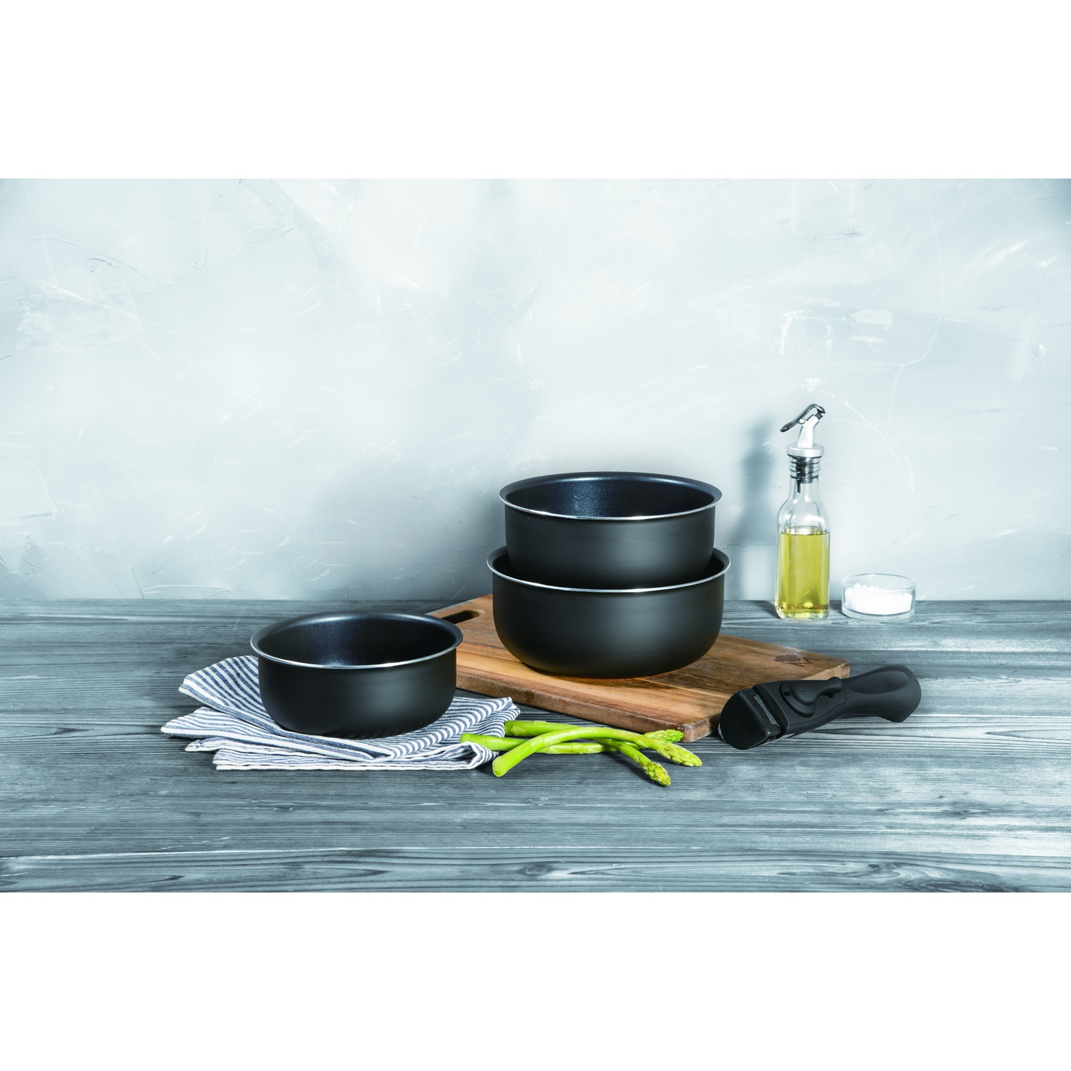 Ollas negras, espárragos, aceite y sal sobre una mesa de madera.
