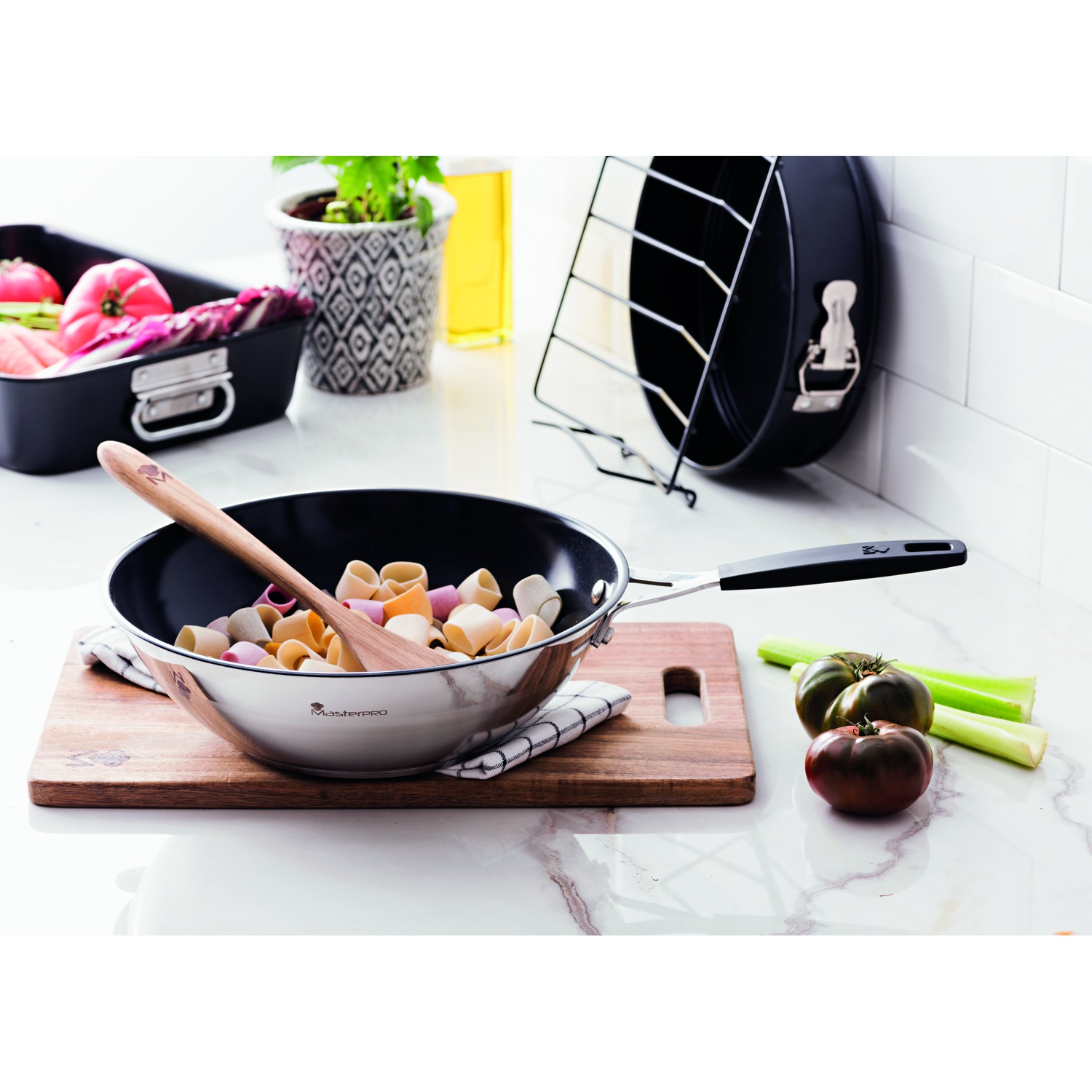 Una sartén con pasta y utensilios de cocina sobre una tabla de cortar.