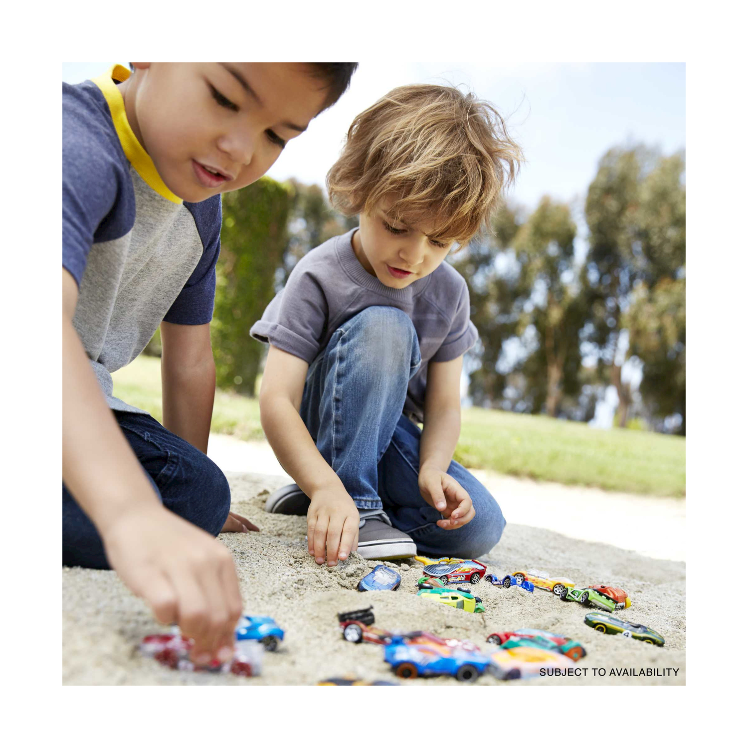 Dwóch chłopców bawi się w piasku wieloma kolorowymi samochodzikami.