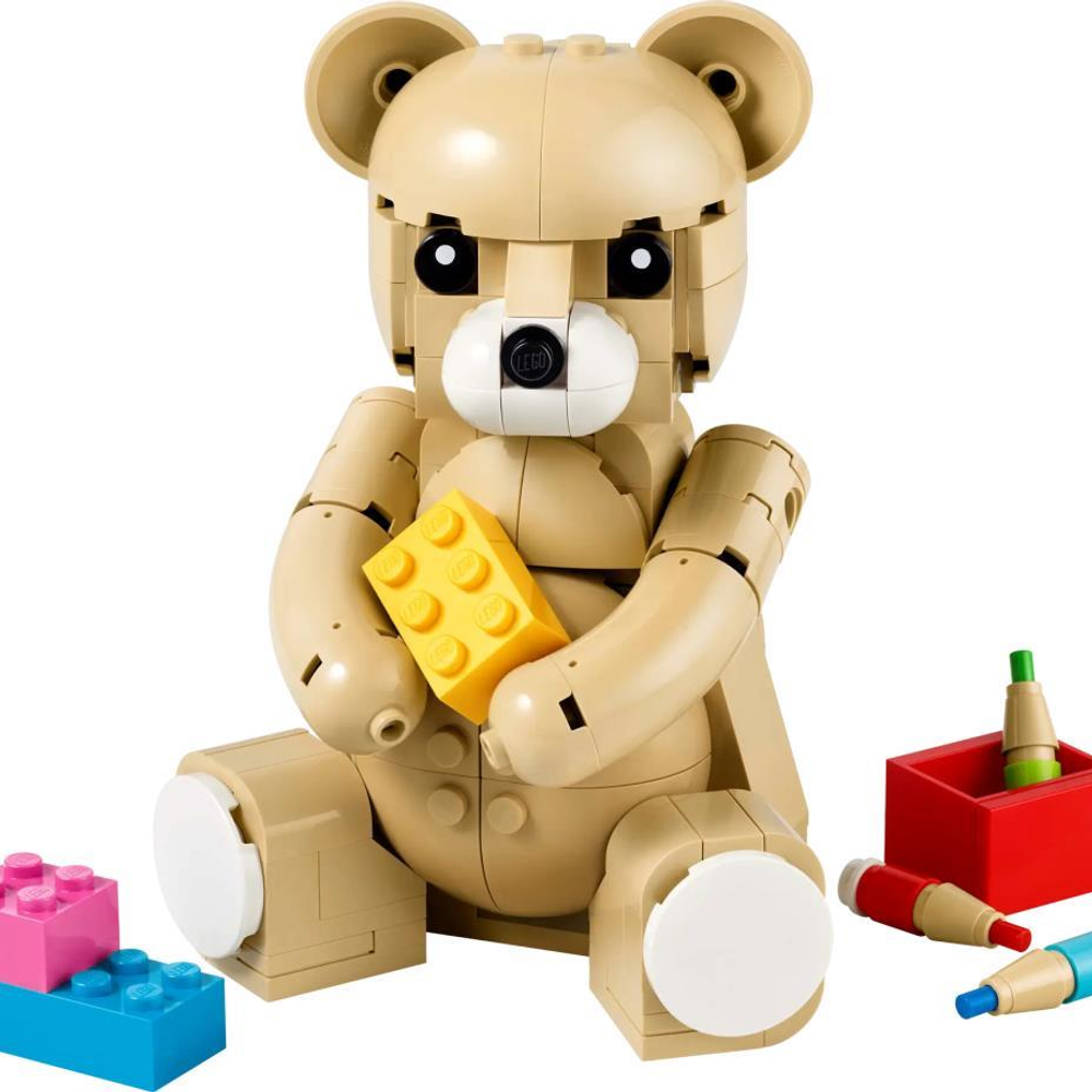 Un orsacchiotto LEGO beige tiene un mattoncino LEGO giallo. Ci sono mattoncini LEGO colorati nelle vicinanze.