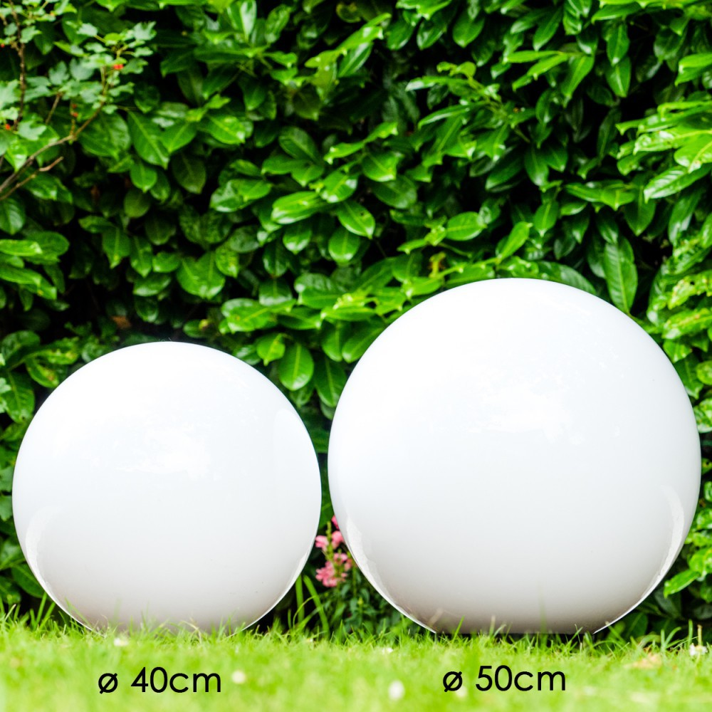 Zwei weiße Kugeln, 40cm und 50cm, stehen im Gras vor grünen Büschen.