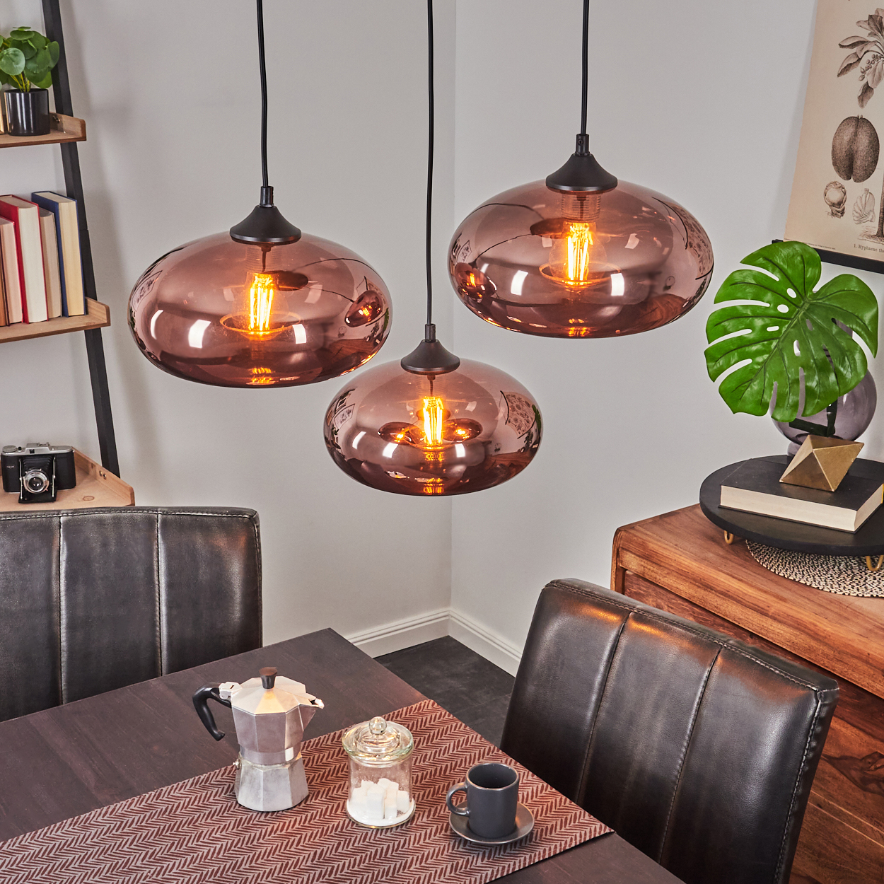 Drei kupferfarbene Pendelleuchten über einem Holztisch mit Kaffeekanne.