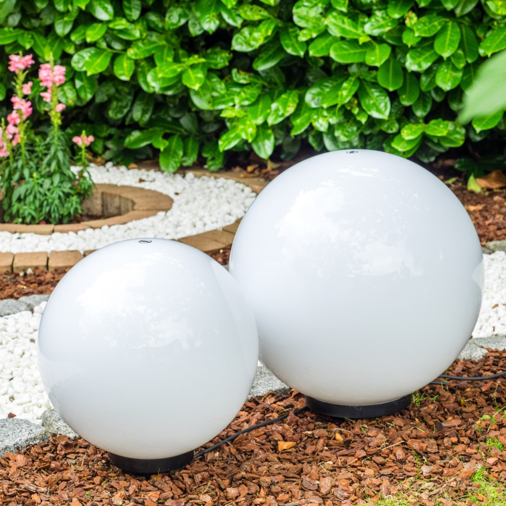 Zwei weiße Kugelleuchten im Garten, mit Pflanzen und Kies im Hintergrund.