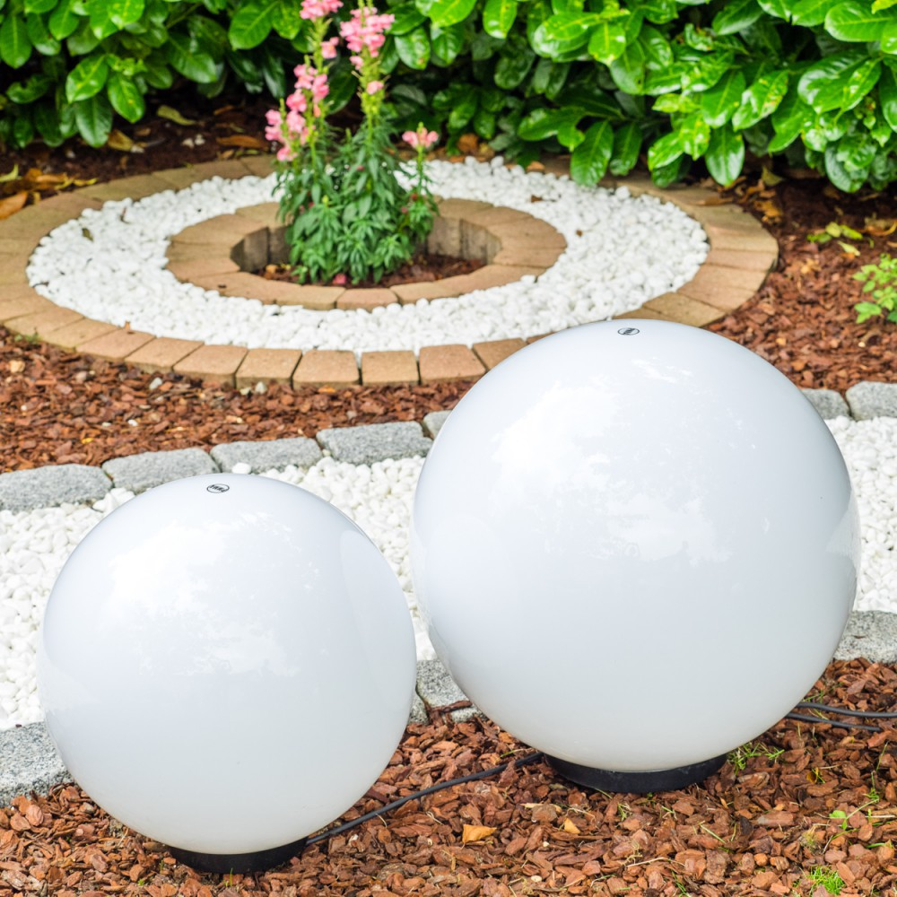 Zwei weiße Kugelleuchten im Garten, umgeben von Kies und Rindenmulch.