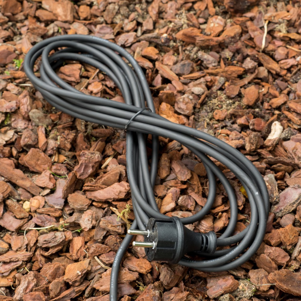 Schwarzes Stromkabel mit Stecker liegt auf Rindenmulch.