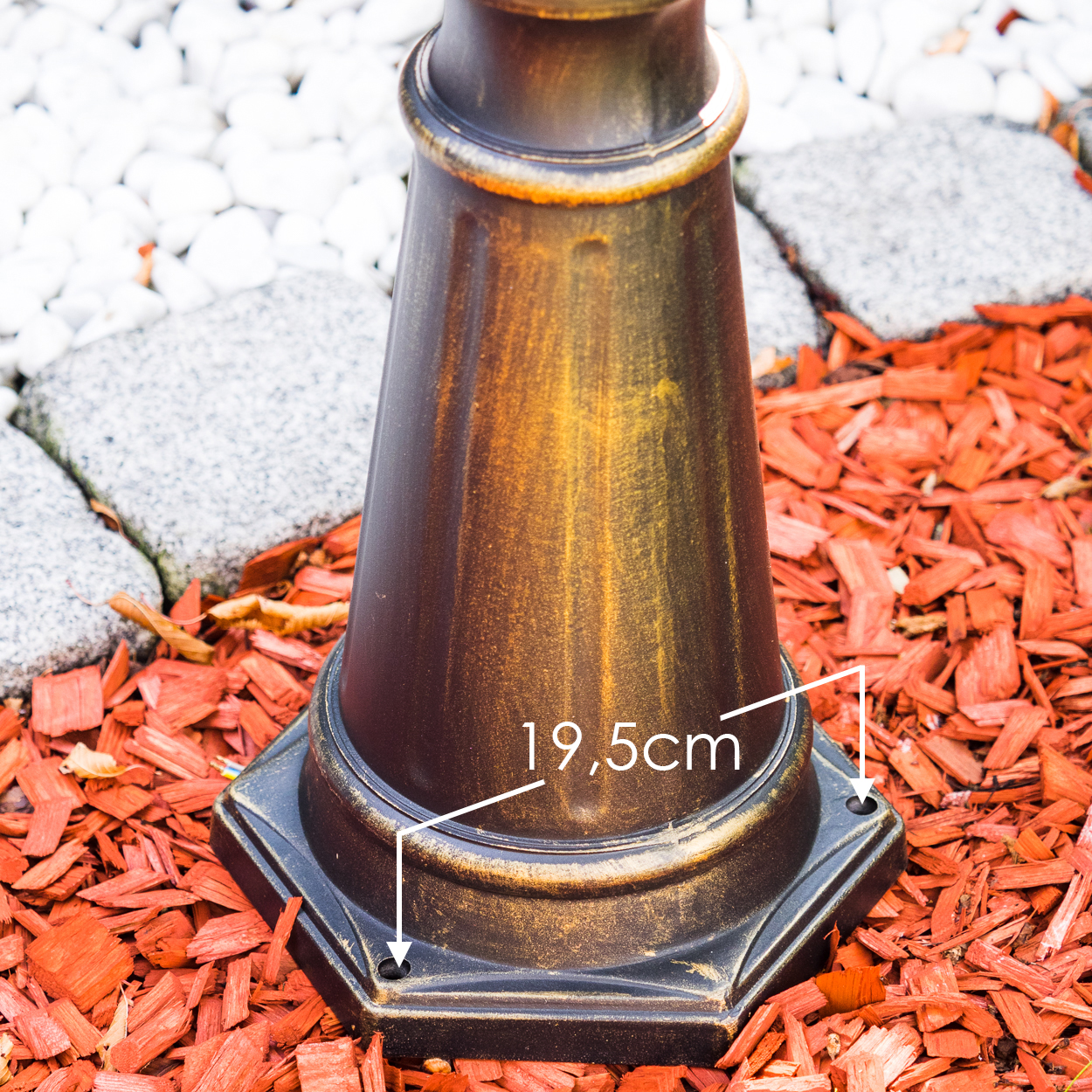 Bronzefarbene Laternenbasis auf rotem Mulch, mit Maßangabe 19,5 cm.