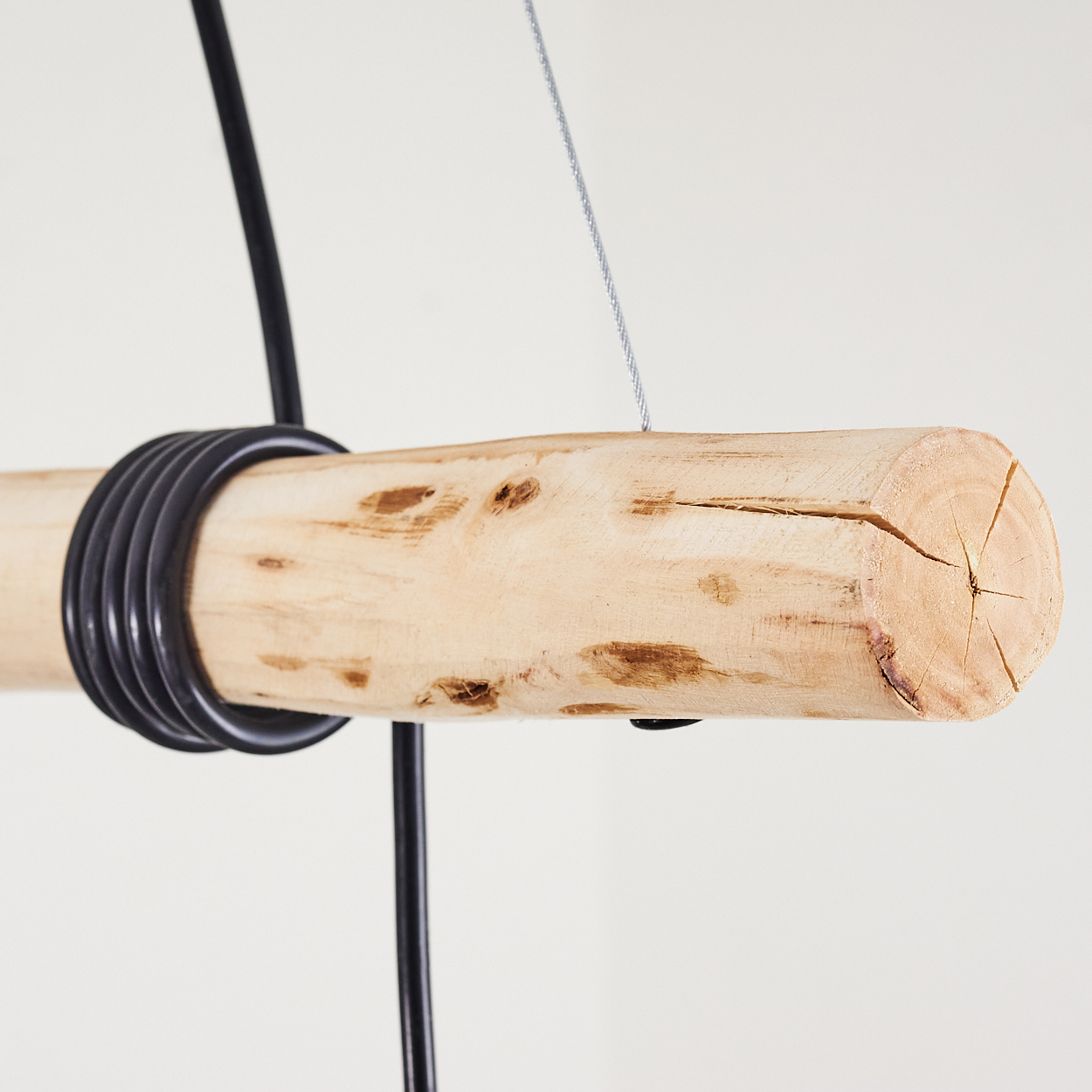 Ein hängendes Stück helles Holz mit schwarzen Kabeln und einem Drahtseil.