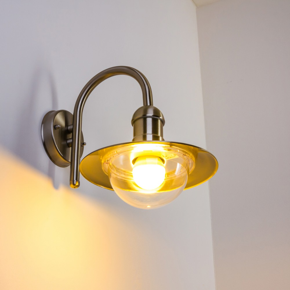 Eine Wandleuchte aus Metall mit Glasglocke und Glühbirne leuchtet hell.