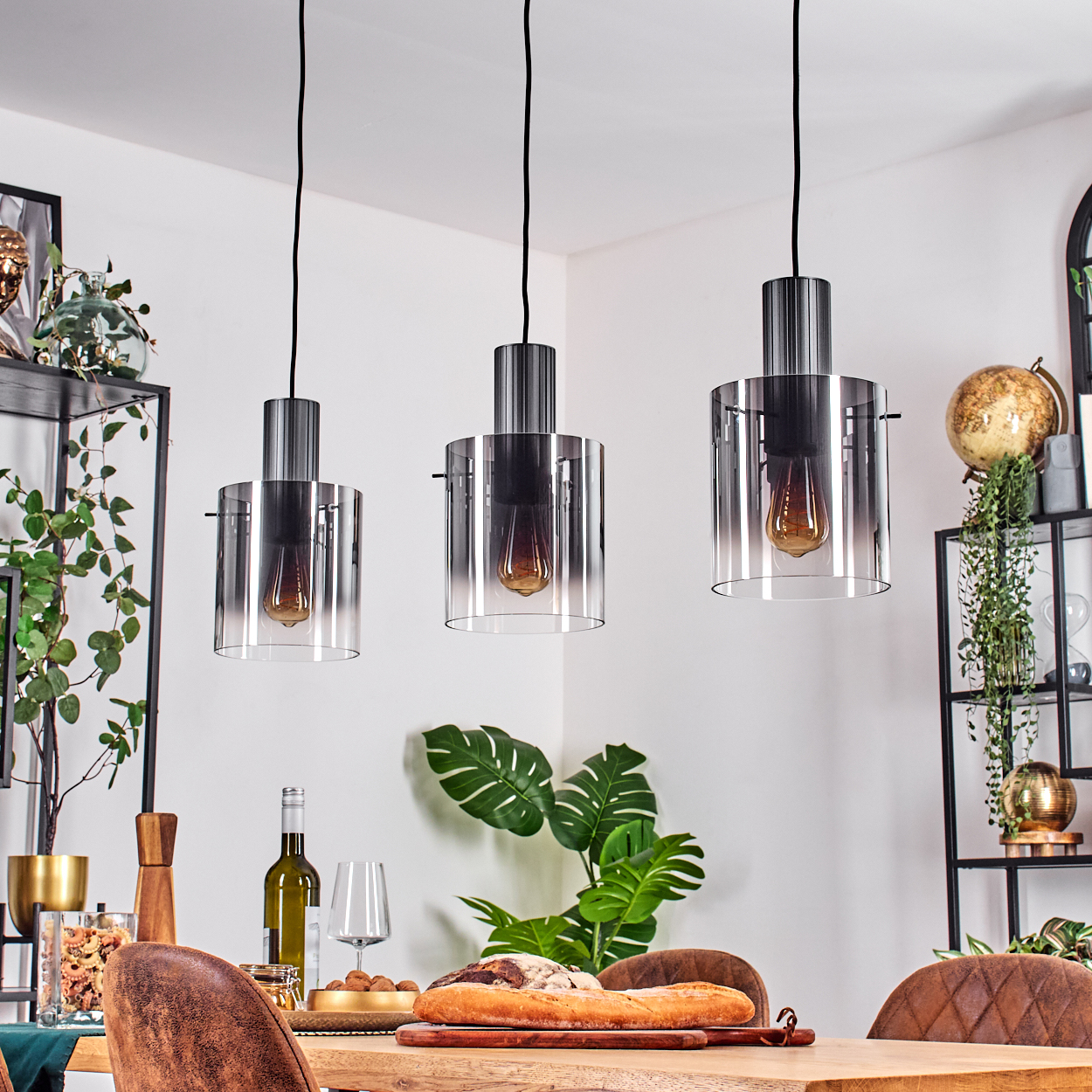 Drei Hängelampen mit Glaszylindern und Glühbirnen über einem Holztisch.