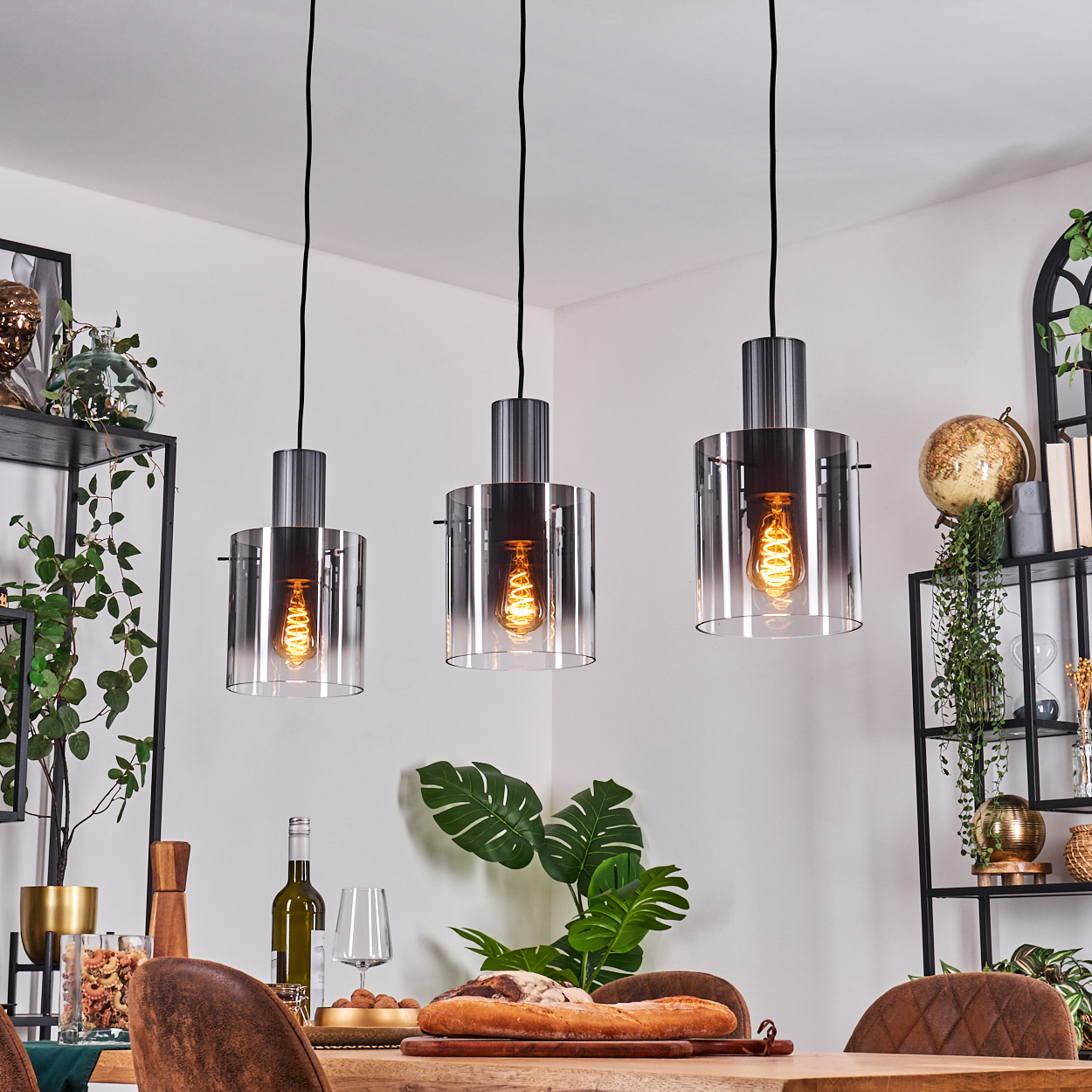 Drei Hängeleuchten mit Glaskolben und Glühbirnen über einem Holztisch.