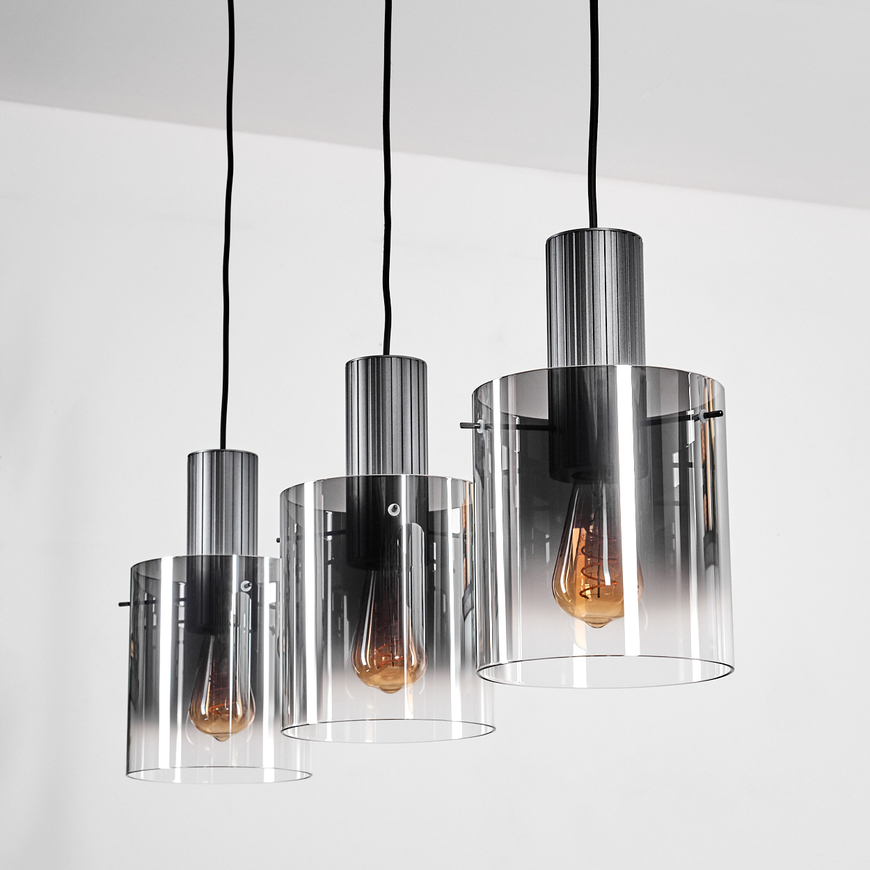 Drei Pendelleuchten mit Glaszylindern und Edison-Glühbirnen.