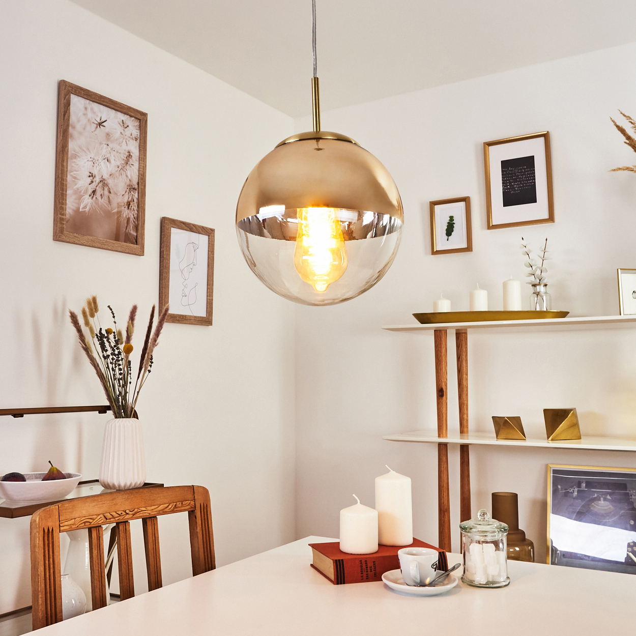 Hängende goldene Lampe über einem Holztisch mit Kerzen und Büchern.