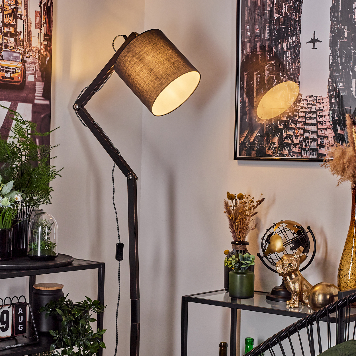 Ein schwarzer Stehlampe beleuchtet eine Ecke mit Kunst und Dekoartikeln.