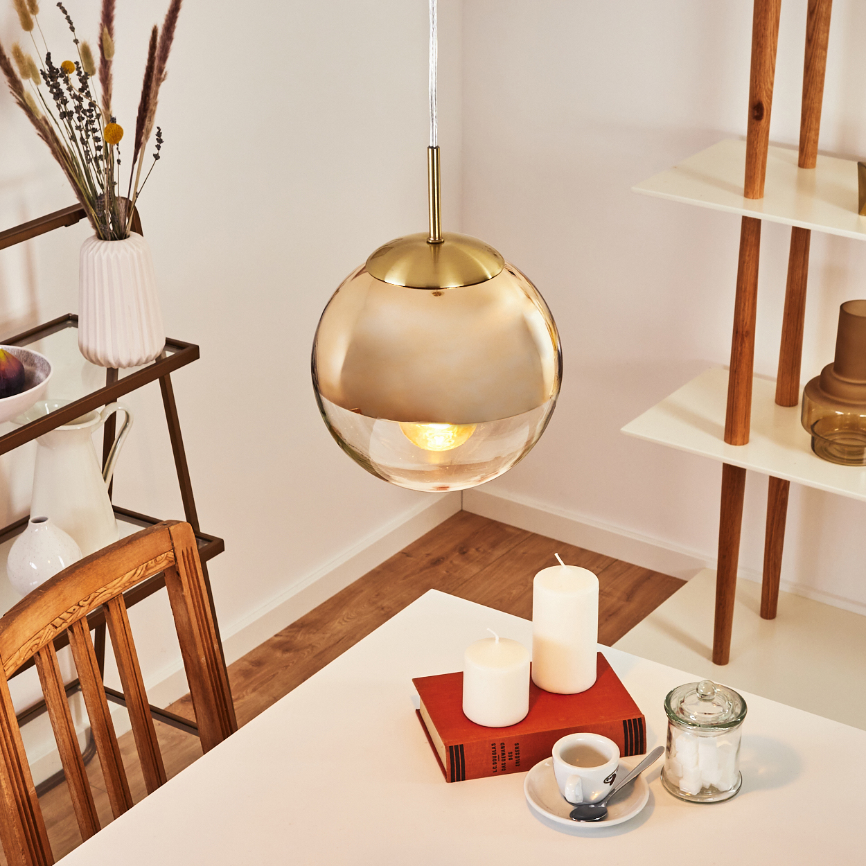 Hängende Lampe über einem Tisch mit Kerzen, Buch, Kaffeetasse und Zuckerwürfeln.