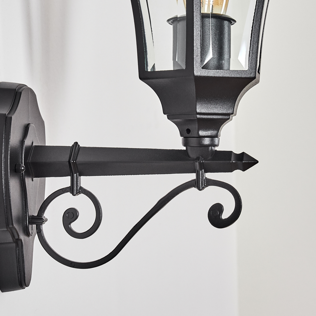 Eine schwarze Wandlampe mit Glas und Glühbirne im Detail.