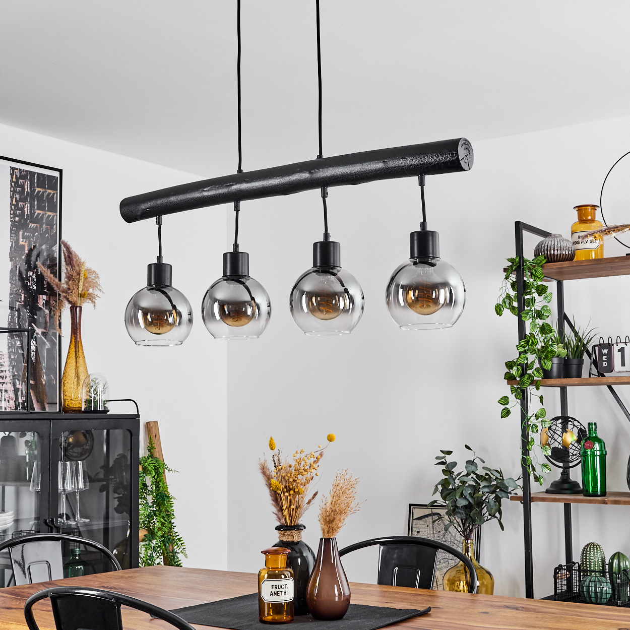 Eine schwarze Pendelleuchte mit vier Glaskugeln hängt über einem Holztisch.