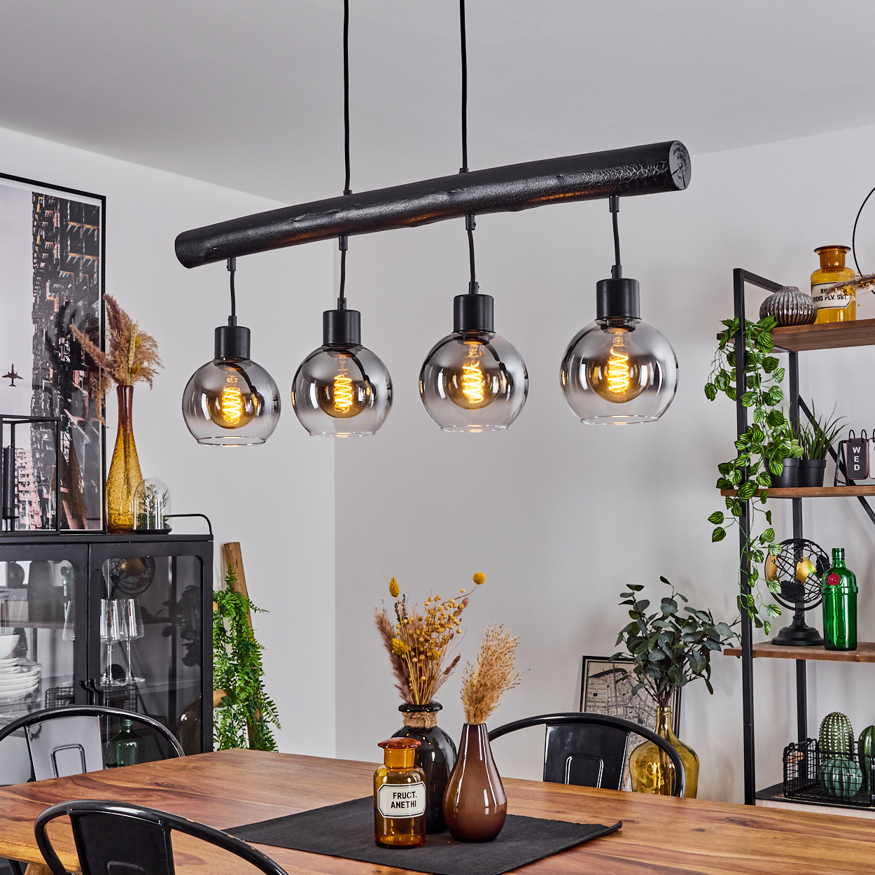 Eine schwarze Pendelleuchte mit vier Rauchglas-Lampenschirmen über einem Holztisch.