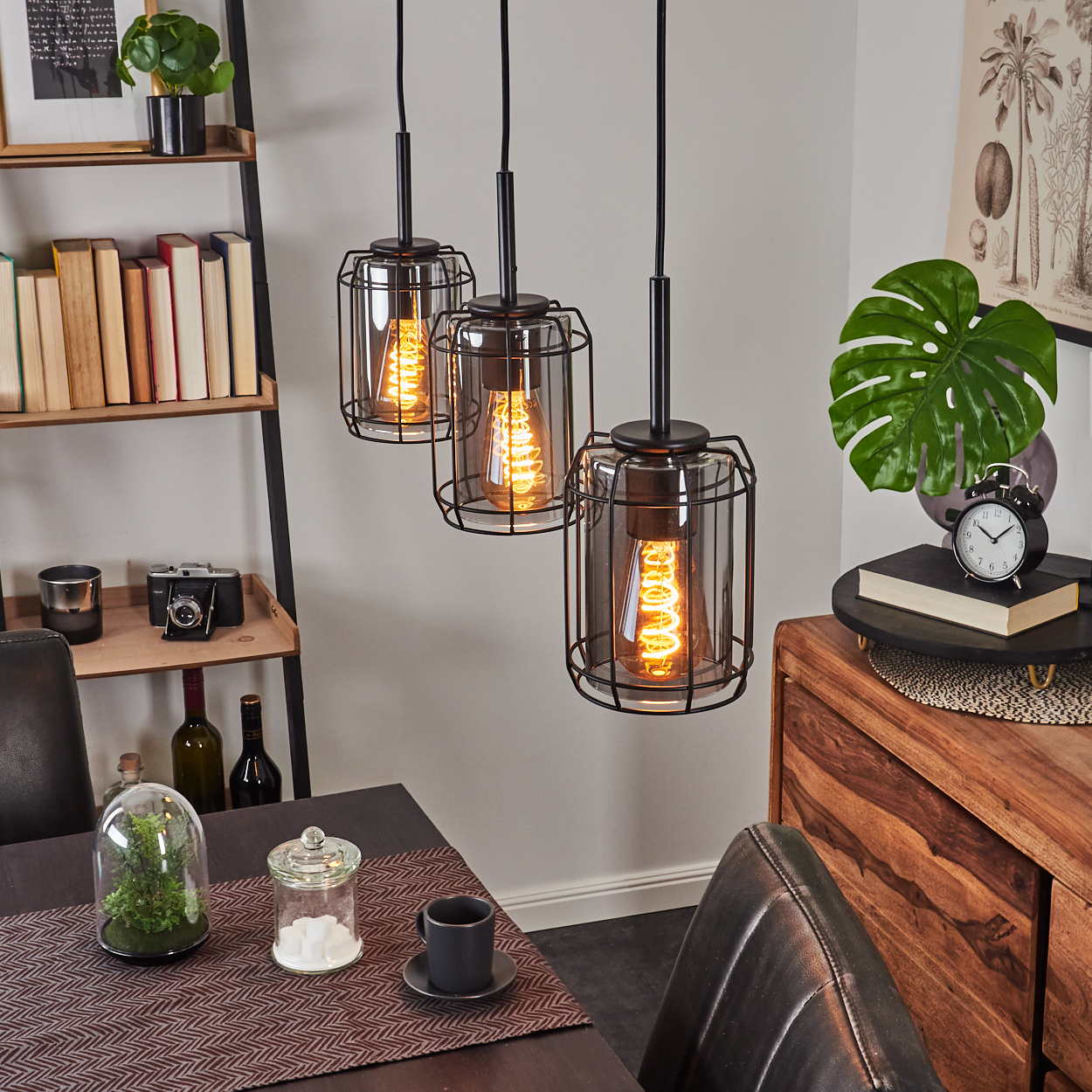 Drei Pendelleuchten mit Käfig-Design über einem Holztisch mit Dekorationen.