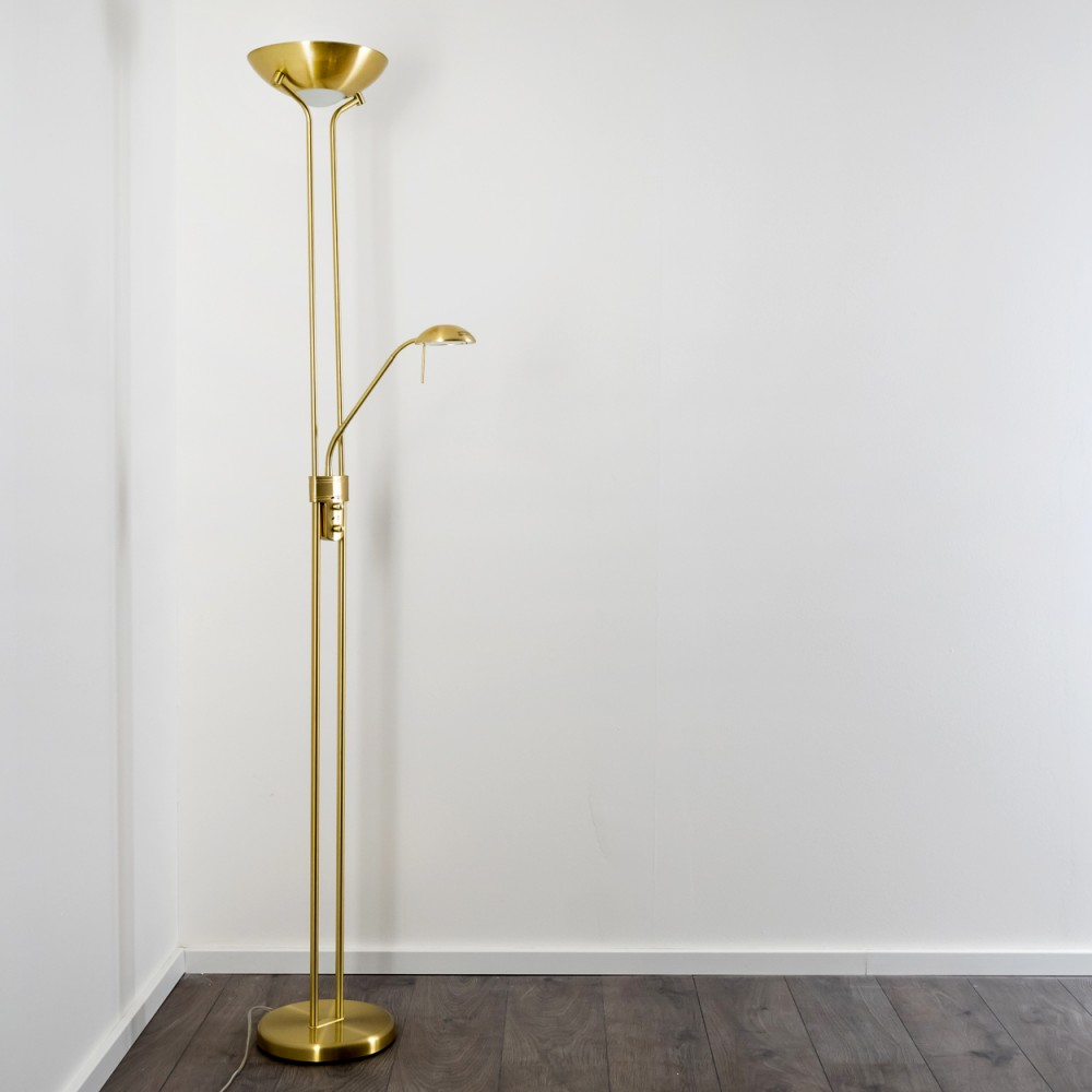 Eine goldene Stehleuchte mit zwei Lichtquellen steht auf einem Holzboden.