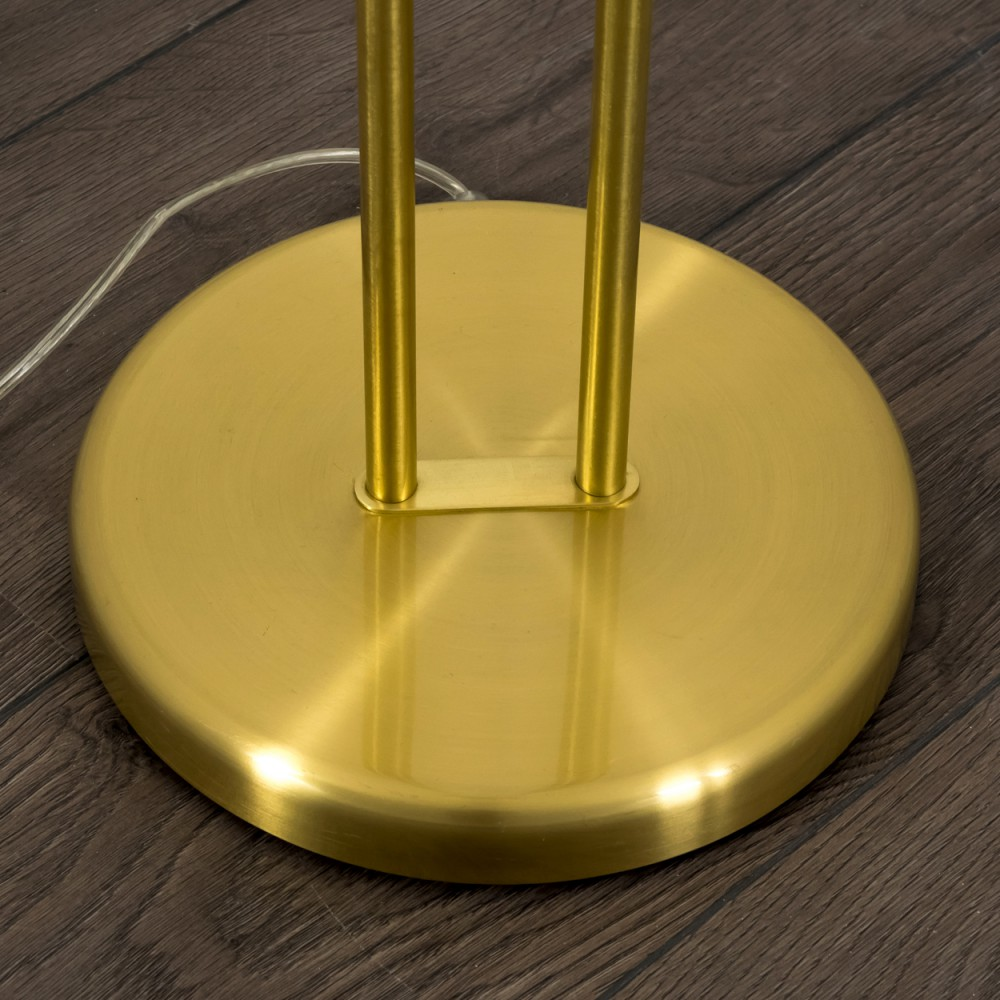 Ein goldener Lampenfuß mit zwei Stangen auf dunklem Holzboden.