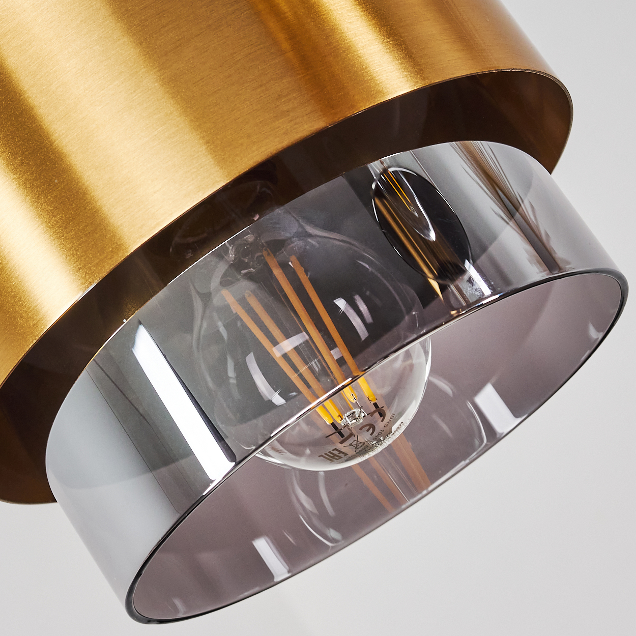 Messingfarbene Lampe mit rauchgrauem Glas und Glühfadenlampe.