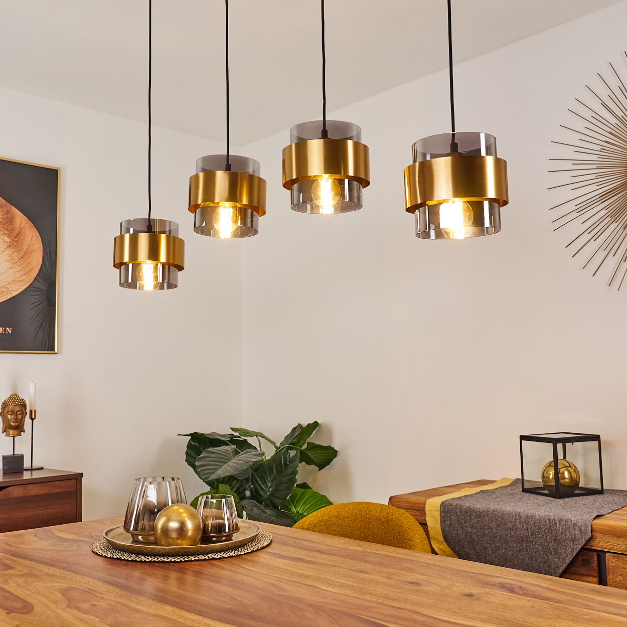 Vier Hängeleuchten mit goldfarbenen Ringen und Rauchglaszylindern über einem Holztisch.