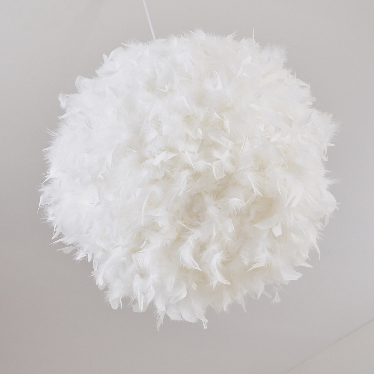 Eine kugelförmige Lampe aus weißen Federn hängt von der Decke.