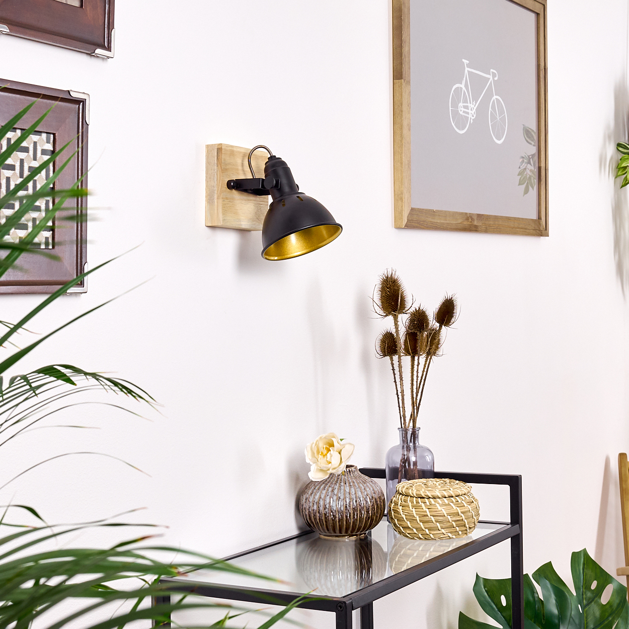 Ein schwarzer Wandspot mit goldenem Inneren hängt über einem Regal mit Deko.