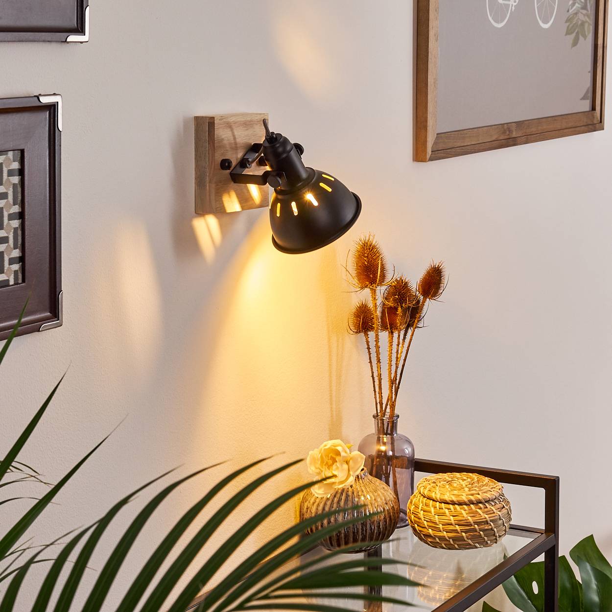 Ein schwarzer Wandspot leuchtet auf Holz. daneben Trockenblumen und Deko.