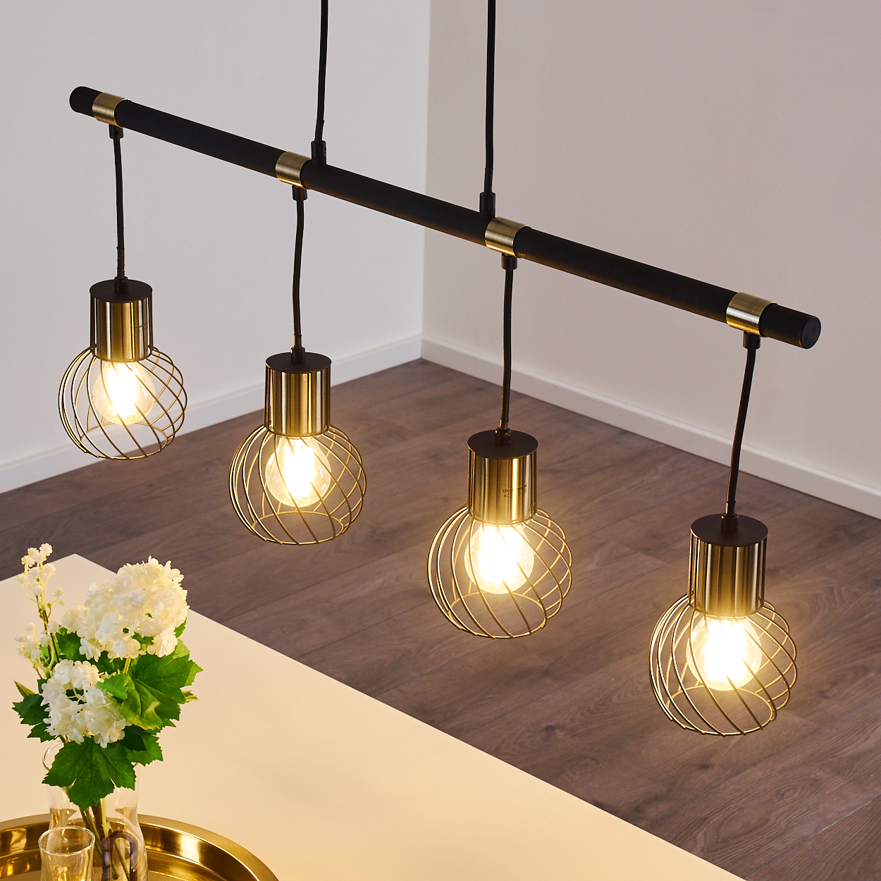 Schwarzer Balken mit vier hängenden Lampen mit goldenen Käfigschirmen und Glühbirnen.