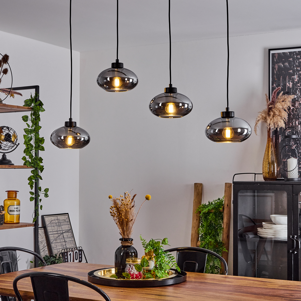 Vier rauchgraue Pendelleuchten über einem Holztisch mit Dekoration.