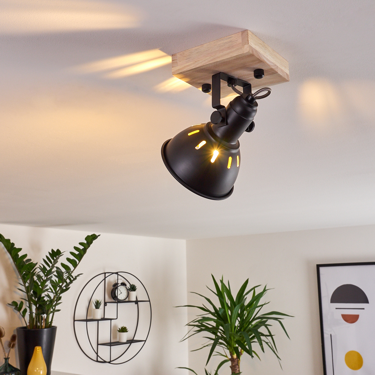 Schwarzer Deckenstrahler mit Holzsockel beleuchtet weiße Decke und Wand.